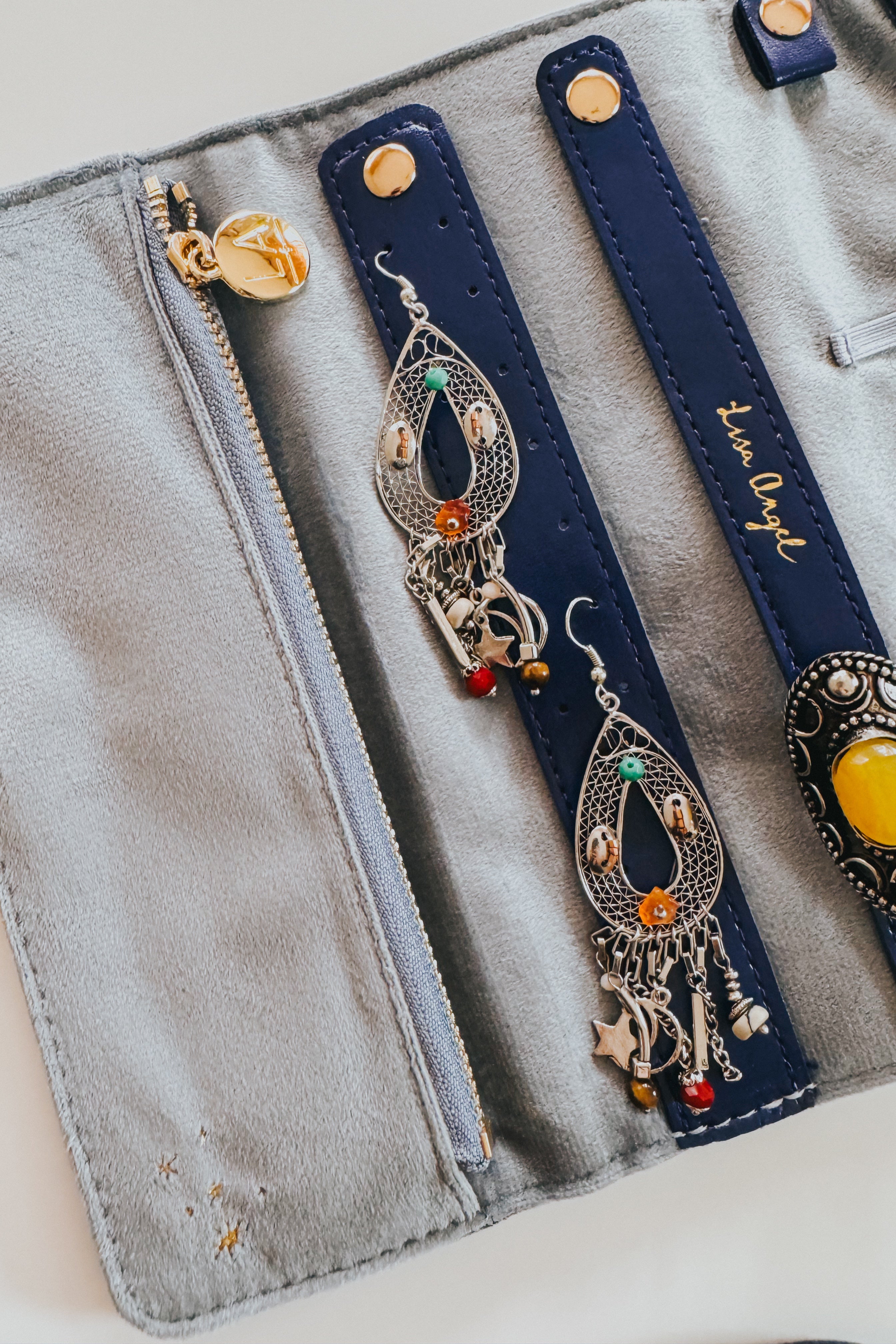 Blue velvet jewelry roll opened displaying silver ornate earrings with colorful beads and charms on navy straps