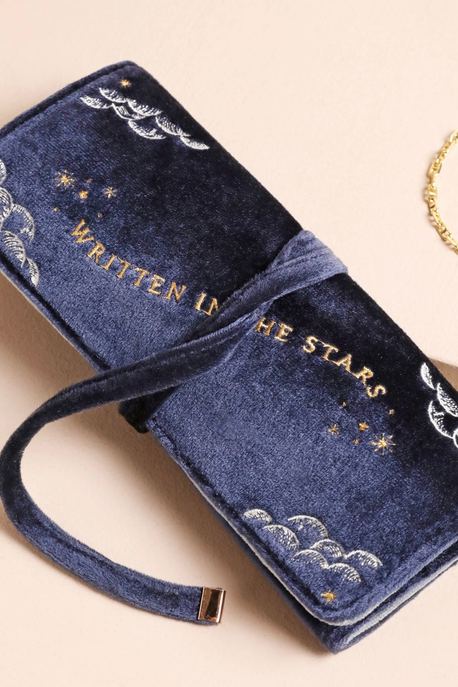 Close-up of navy velvet jewelry roll with celestial embroidery and gold text "Written in the stars" on neutral background