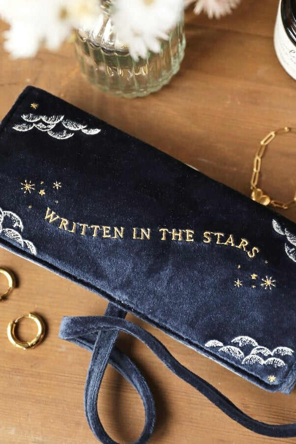 Close-up of plush velvet celestial jewelry roll in deep silver with gold embroidery and tied straps on wood surface