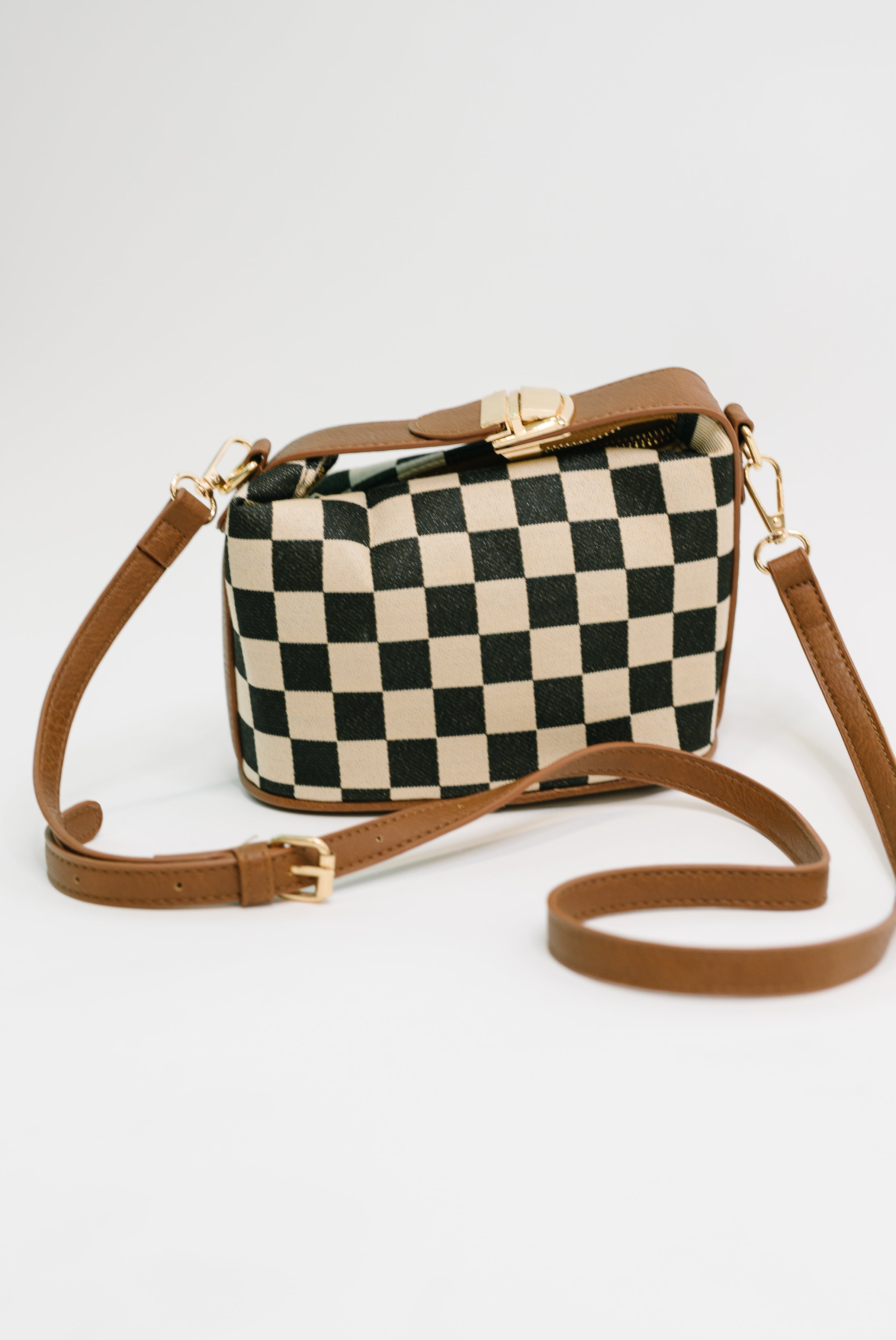 Crossbody bag with black and white check pattern and brown leather straps against a plain background