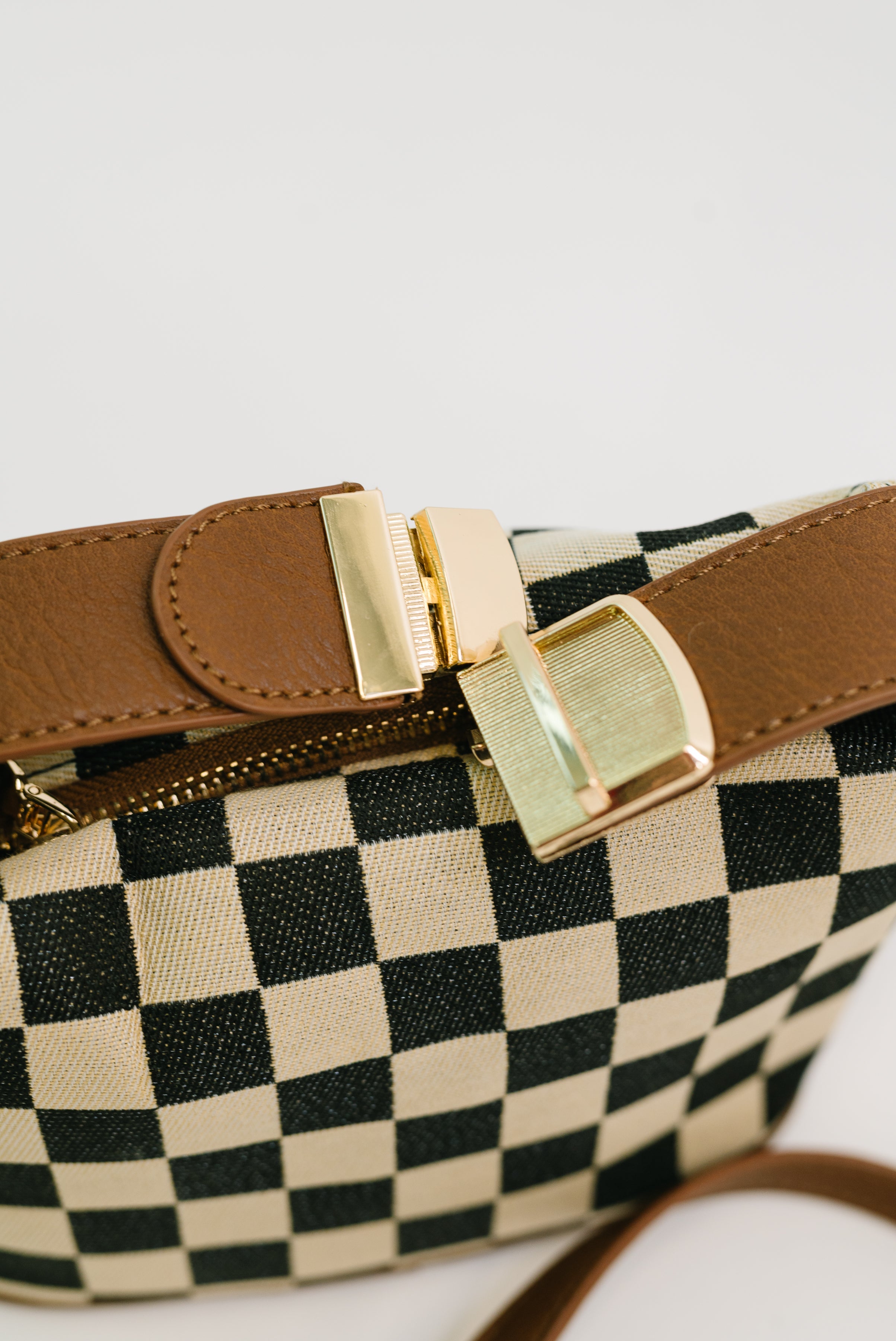 Close-up of black and white checkered crossbody bag with brown leather strap and gold-tone buckle hardware