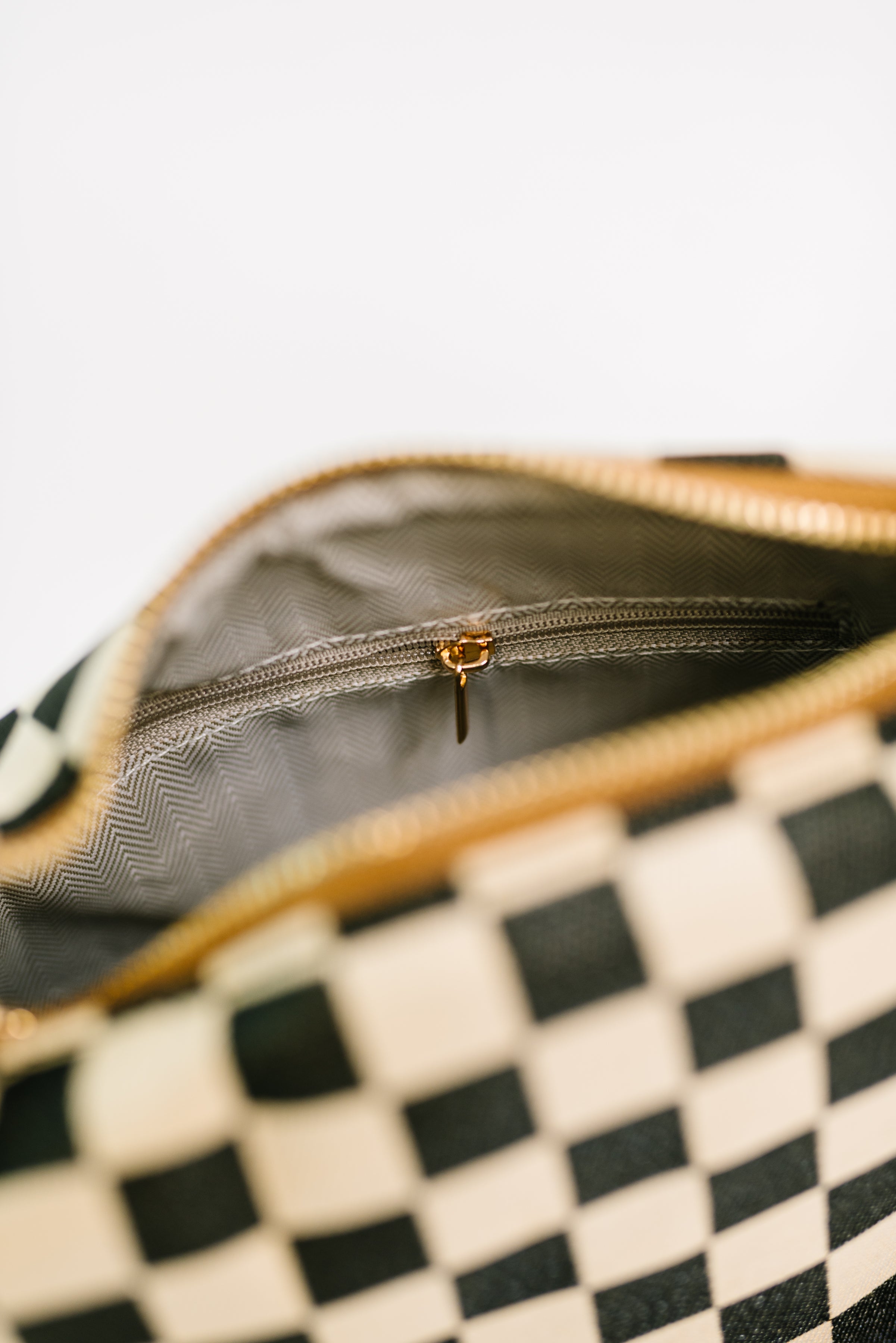Close-up of black and white checkered crossbody bag showing the interior zipper pocket with gold pull detail
