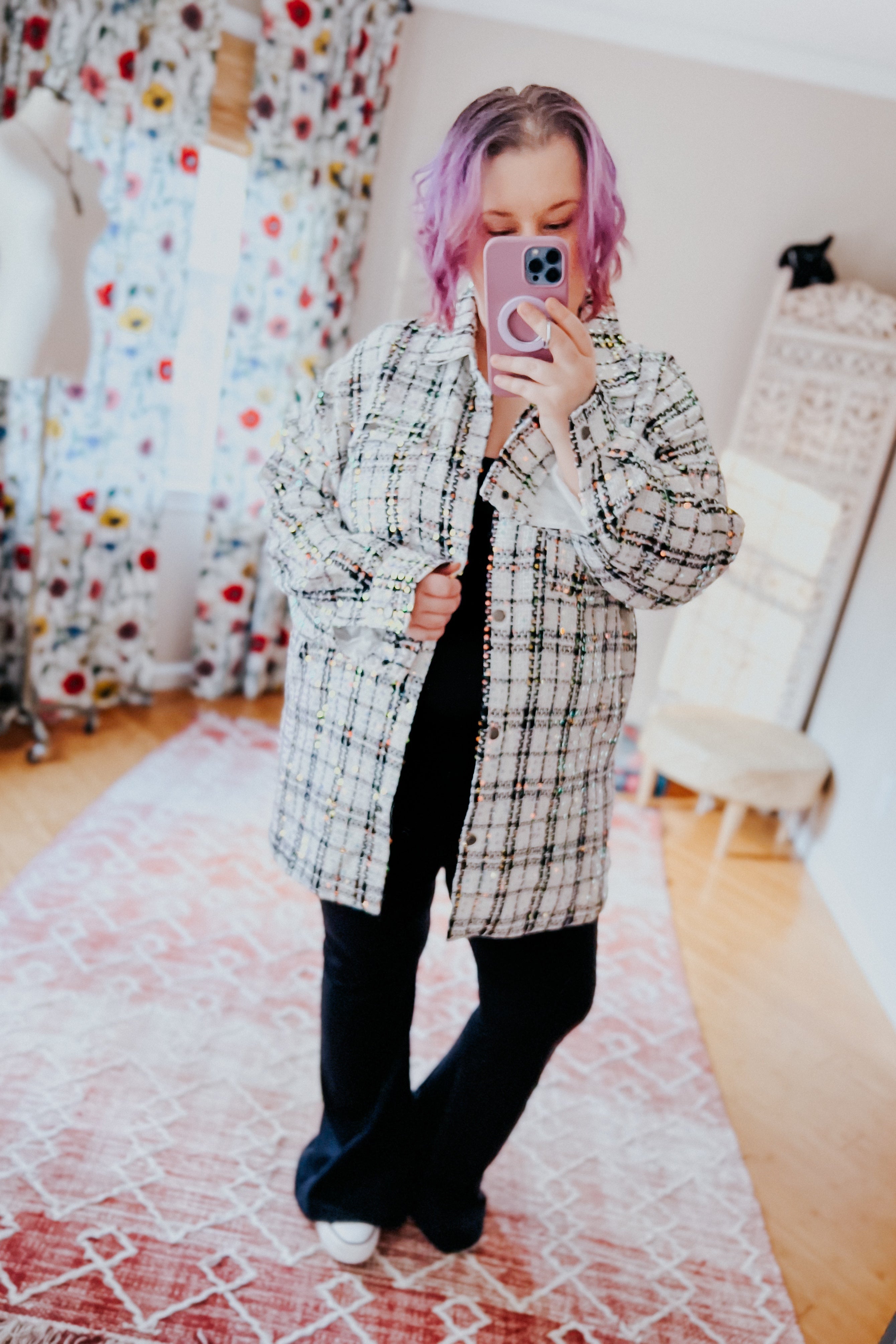 Woman with purple hair wearing white sequin plaid shacket over black outfit taking mirror selfie indoors