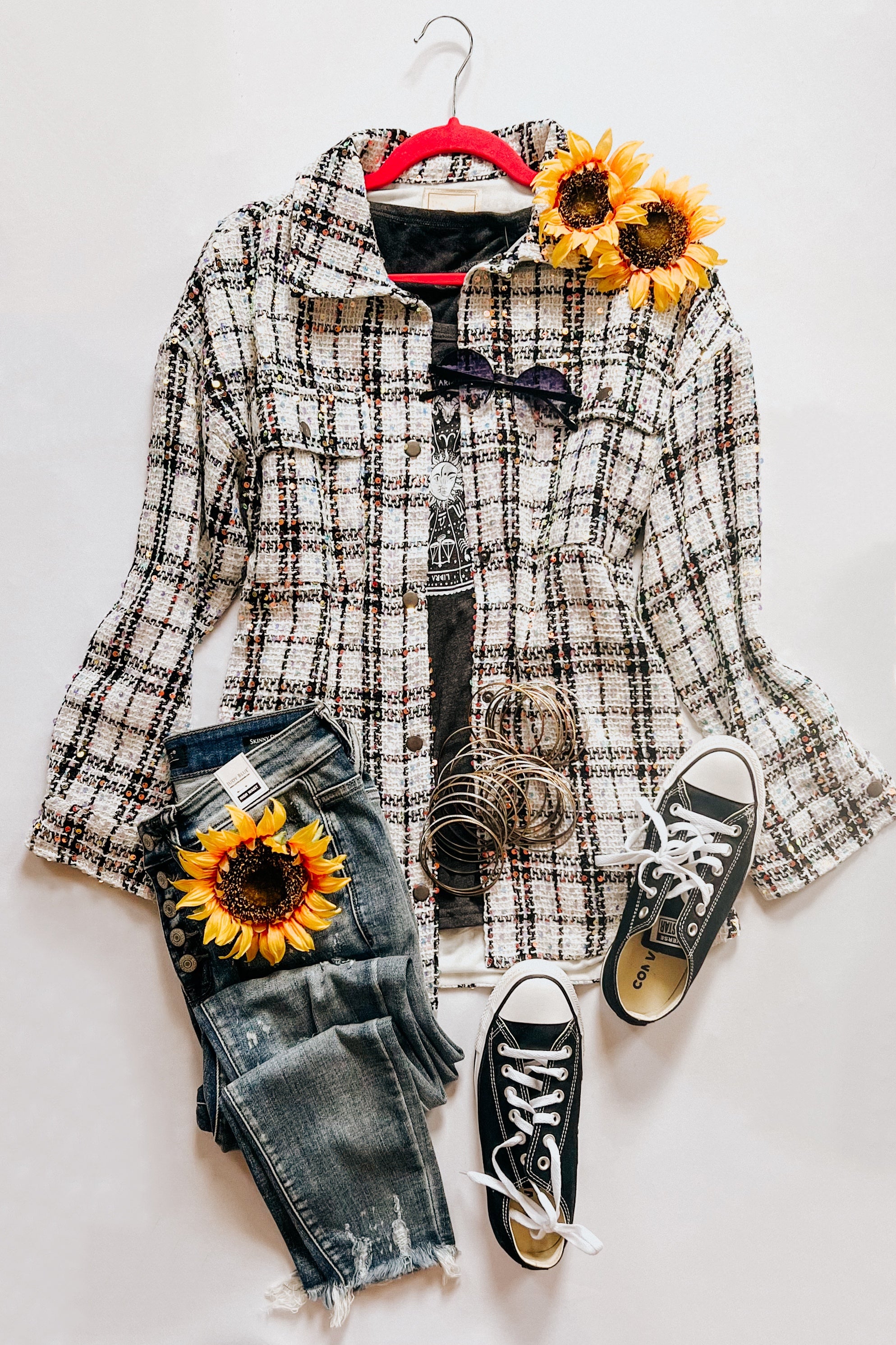 White plaid sequin shacket styled with distressed denim jeans, black sneakers, layered bracelets, and sunflower accents on white background