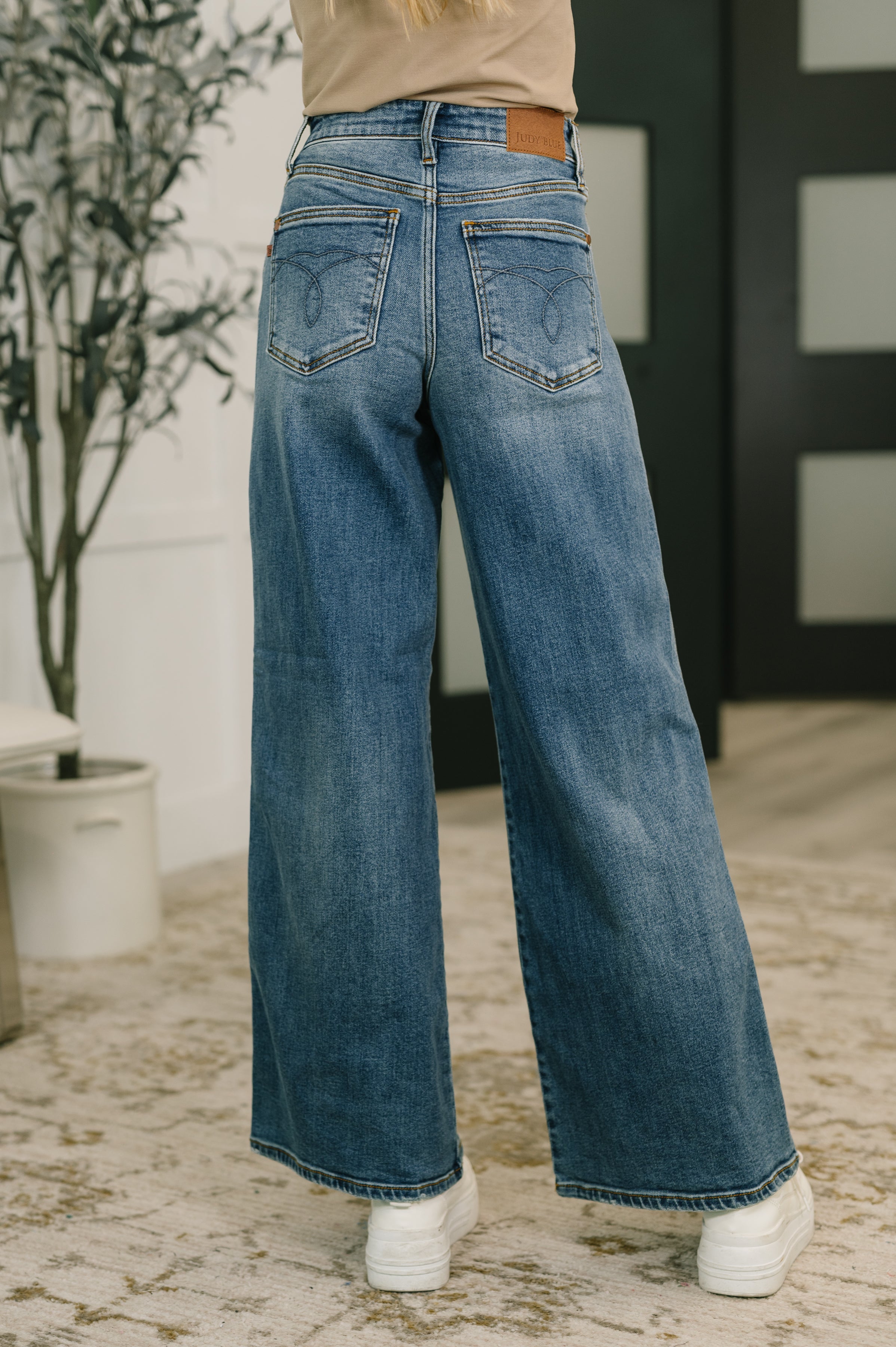 Back view of high waist blue wide leg jeans paired with white sneakers in cozy indoor setting
