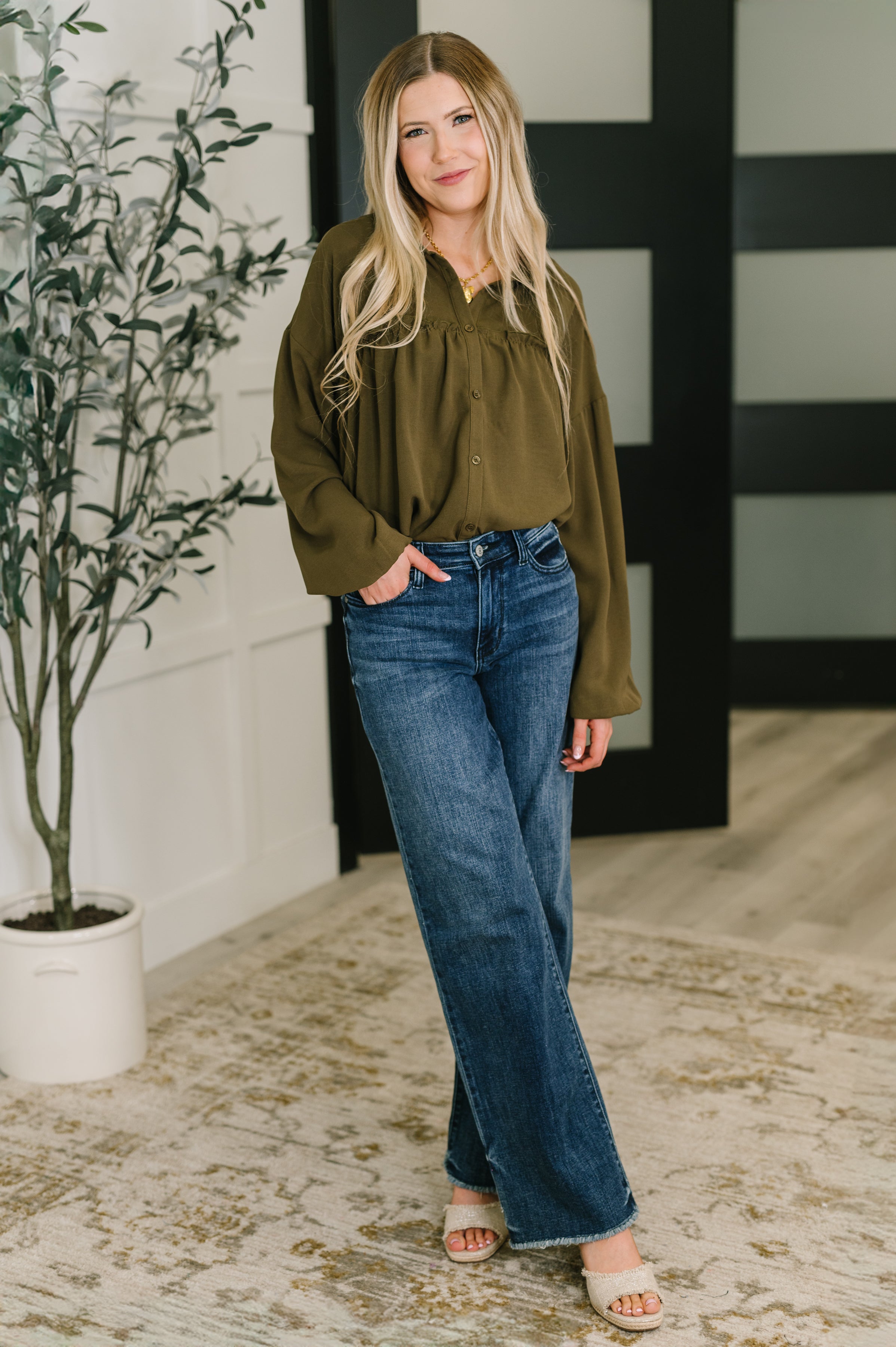 Woman wearing oversized olive button-down blouse paired with high-waisted wide-leg blue jeans indoors