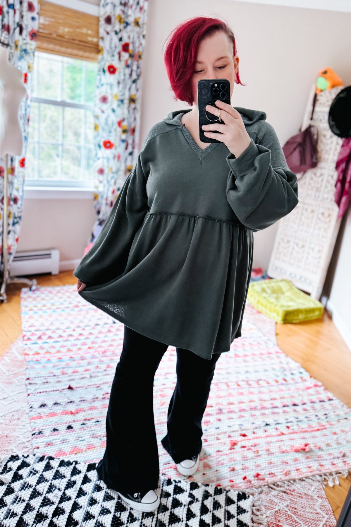 Woman taking a bedroom mirror selfie in a teal hooded V neck pullover with gathered peplum and balloon sleeves styled with black leggings and sneakers
