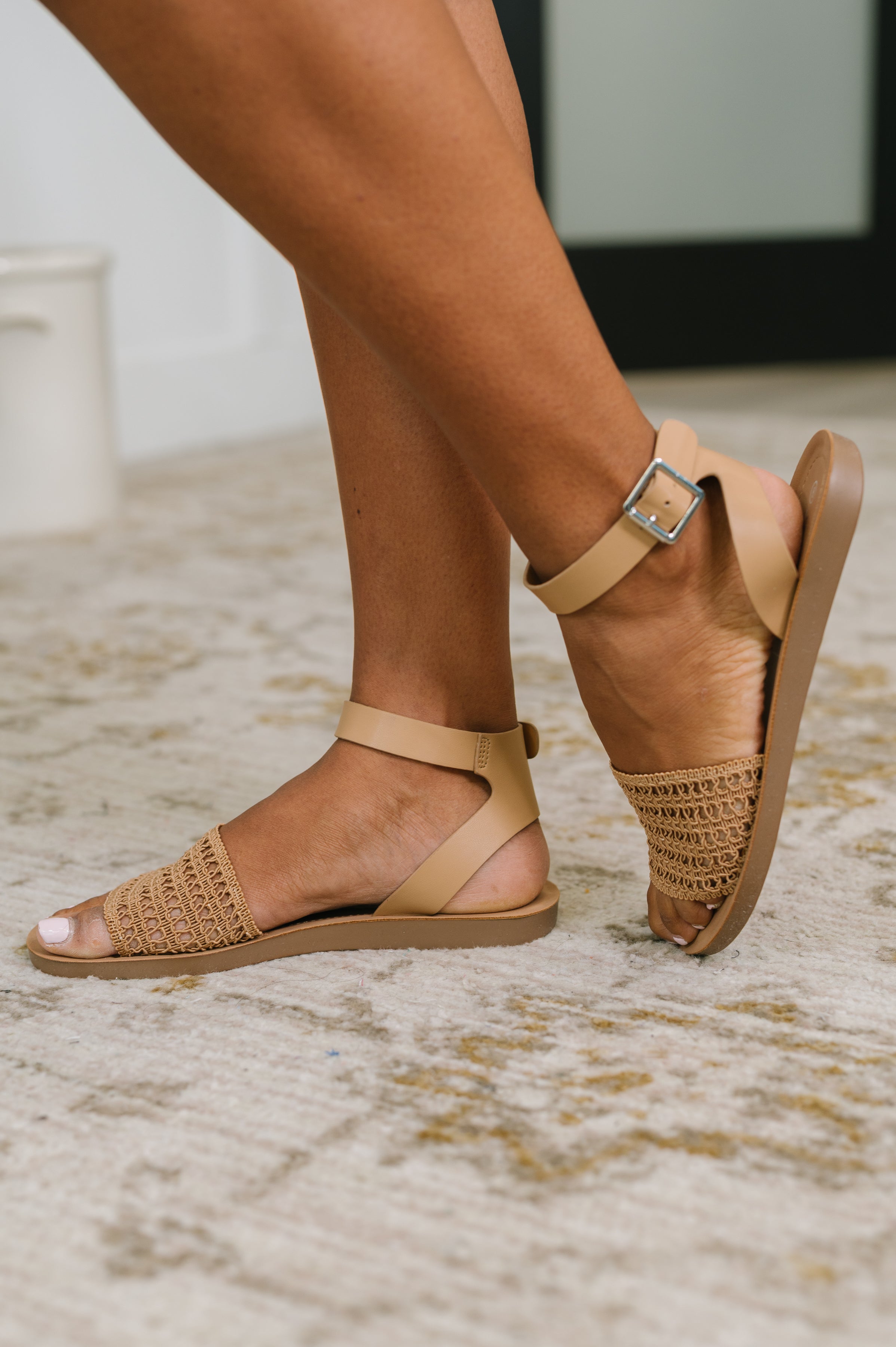 Camel sandal with woven front and ankle strap featuring a silver buckle on a model's feet indoors