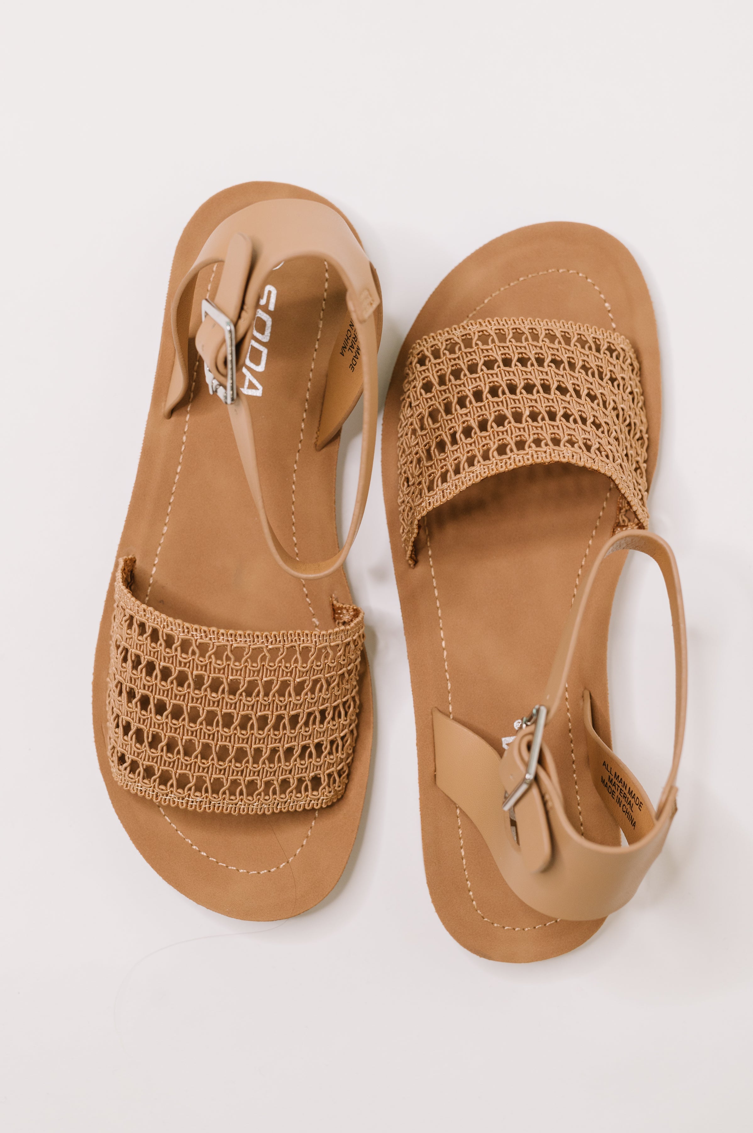 Pair of camel sandals featuring woven front straps and adjustable ankle buckles on a flat sole in a relaxed style