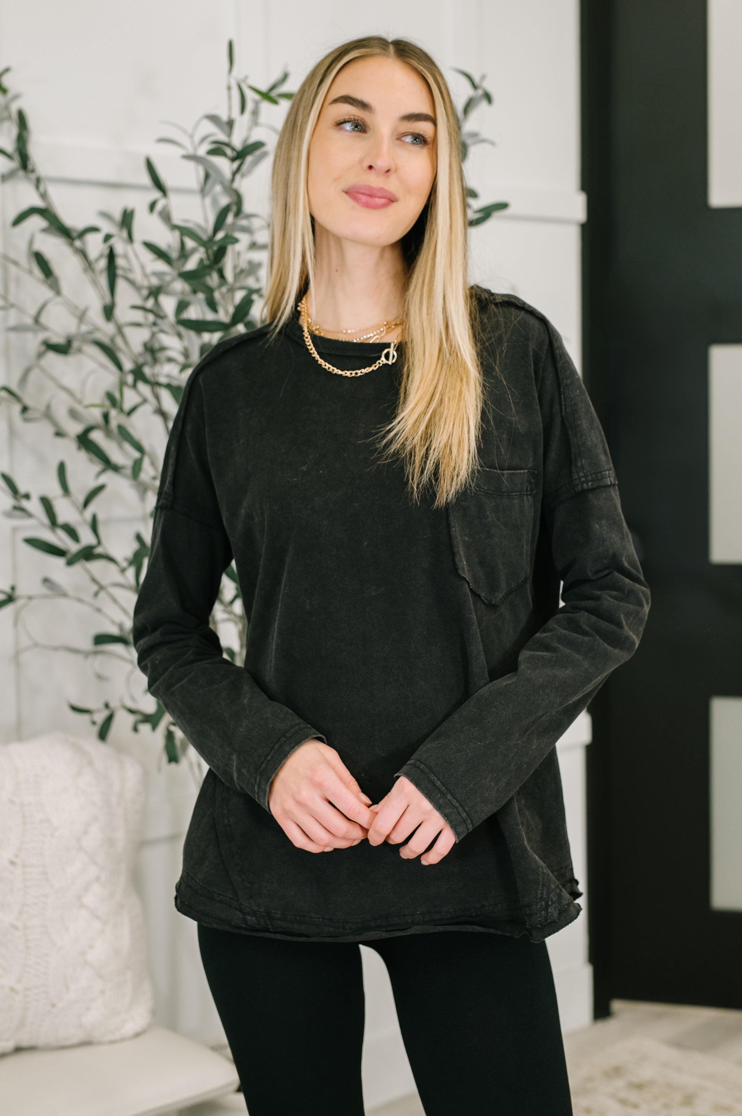 Woman wearing a black long-sleeve shirt with a breast pocket and black leggings in an indoor setting.