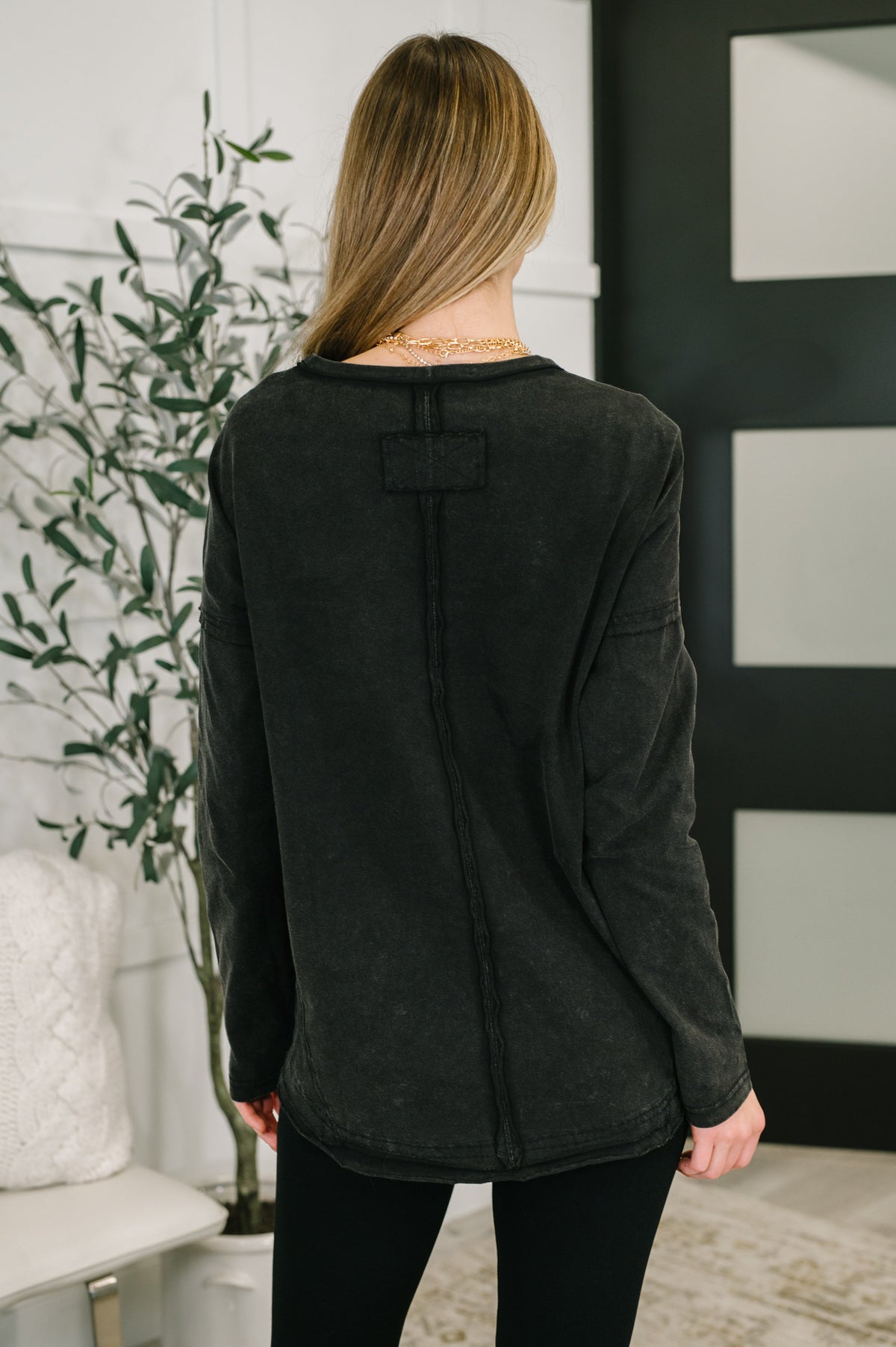 Woman viewed from behind wearing a black long sleeve exposed seam top with black leggings in a stylish home interior