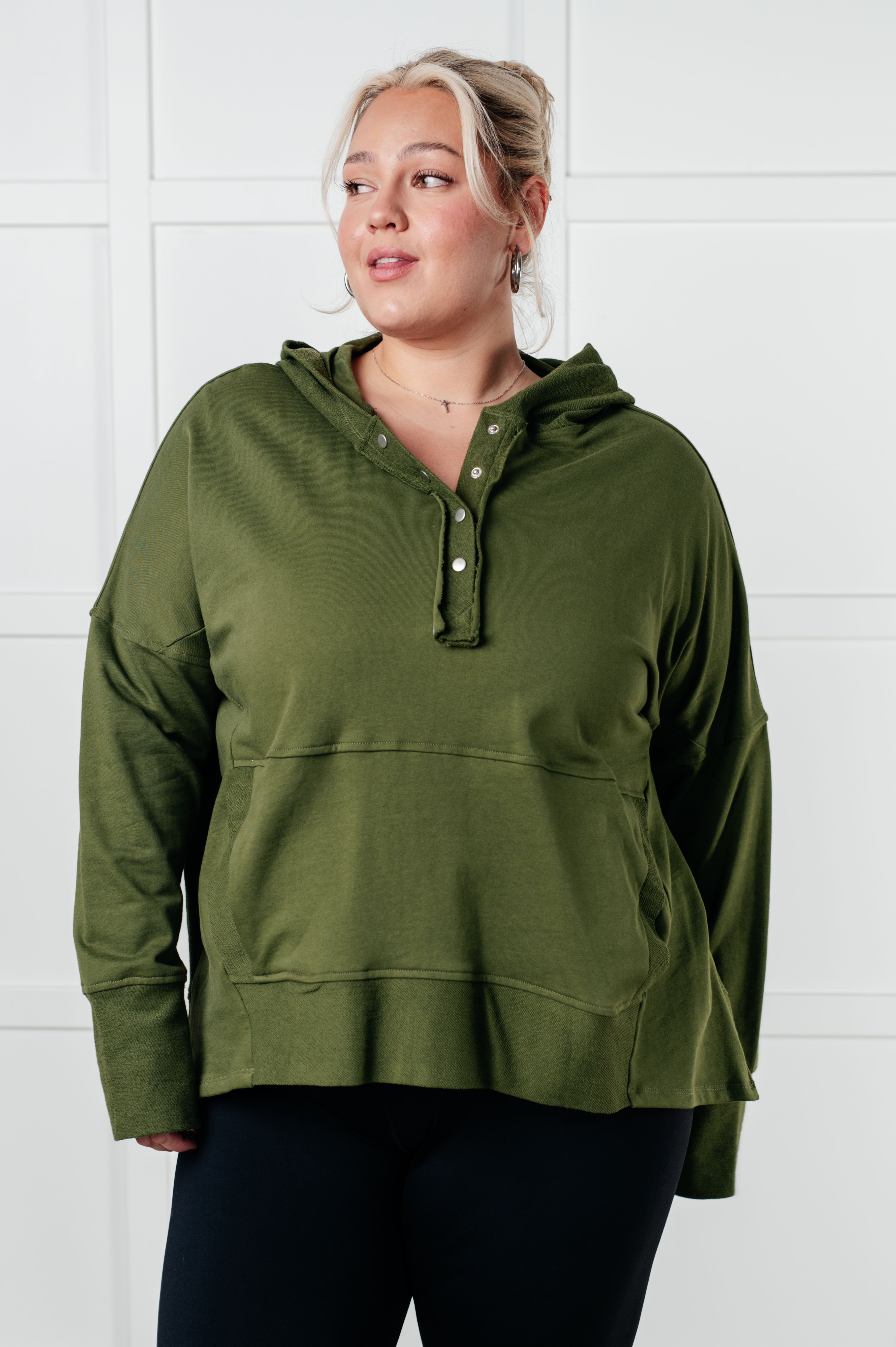 Woman wearing relaxed-fit green hooded pullover with snap buttons in casual indoor setting smiling gently