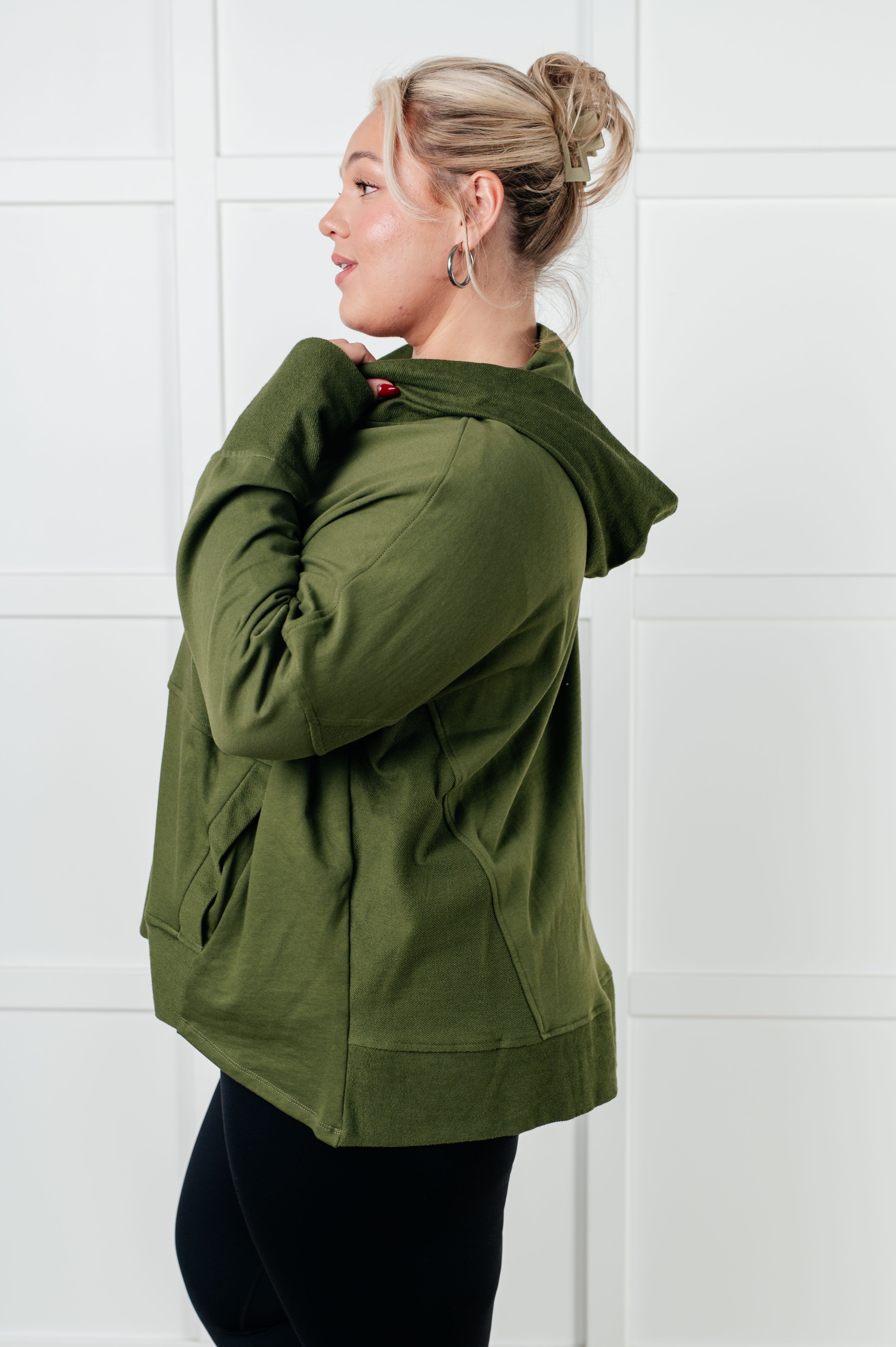 Plus-size woman wearing green snug hooded pullover with relaxed fit and side pockets against light paneled wall
