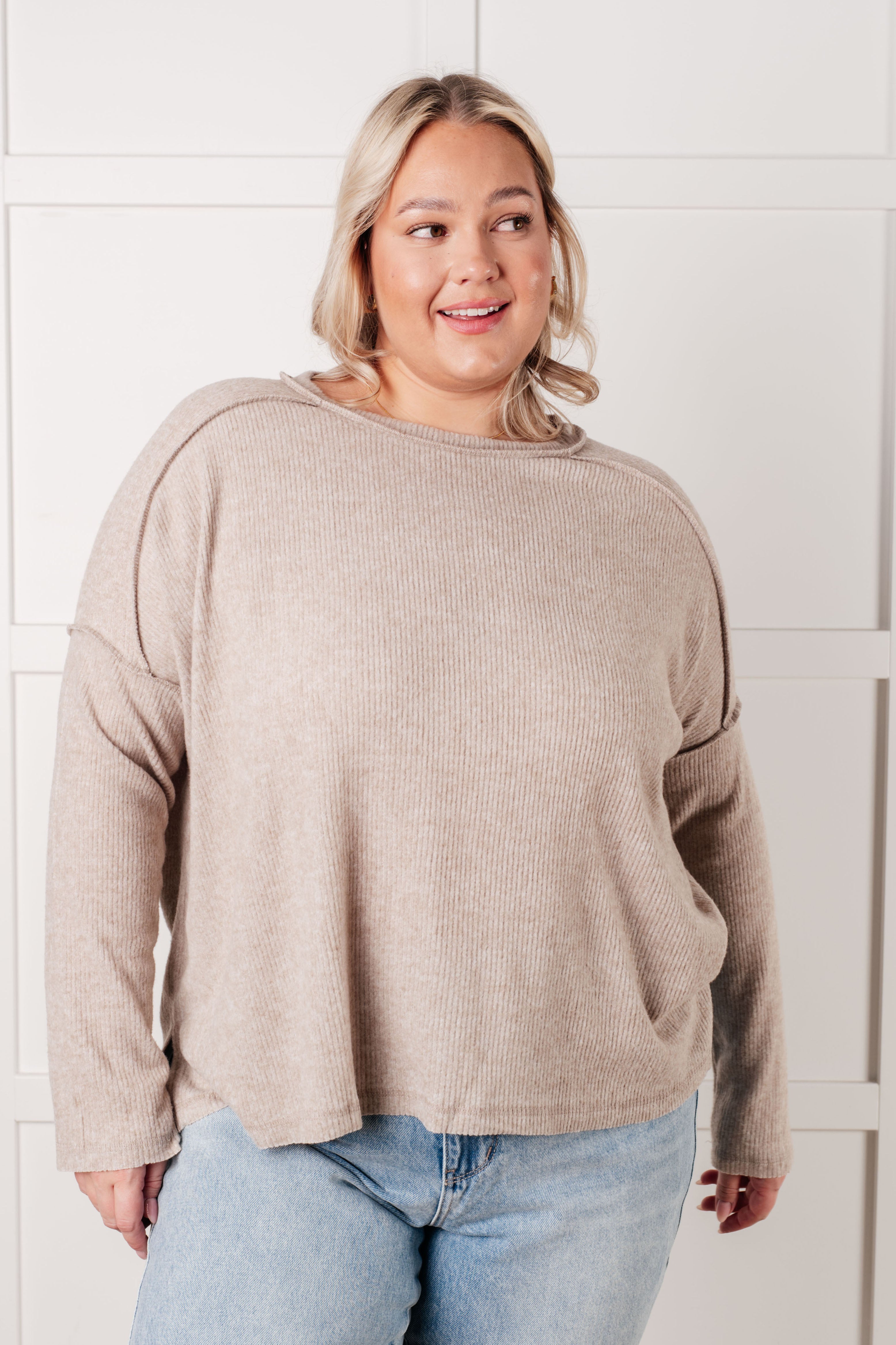 Smiling plus-size woman wearing relaxed heather mocha ribbed sweater paired with light blue jeans in bright space