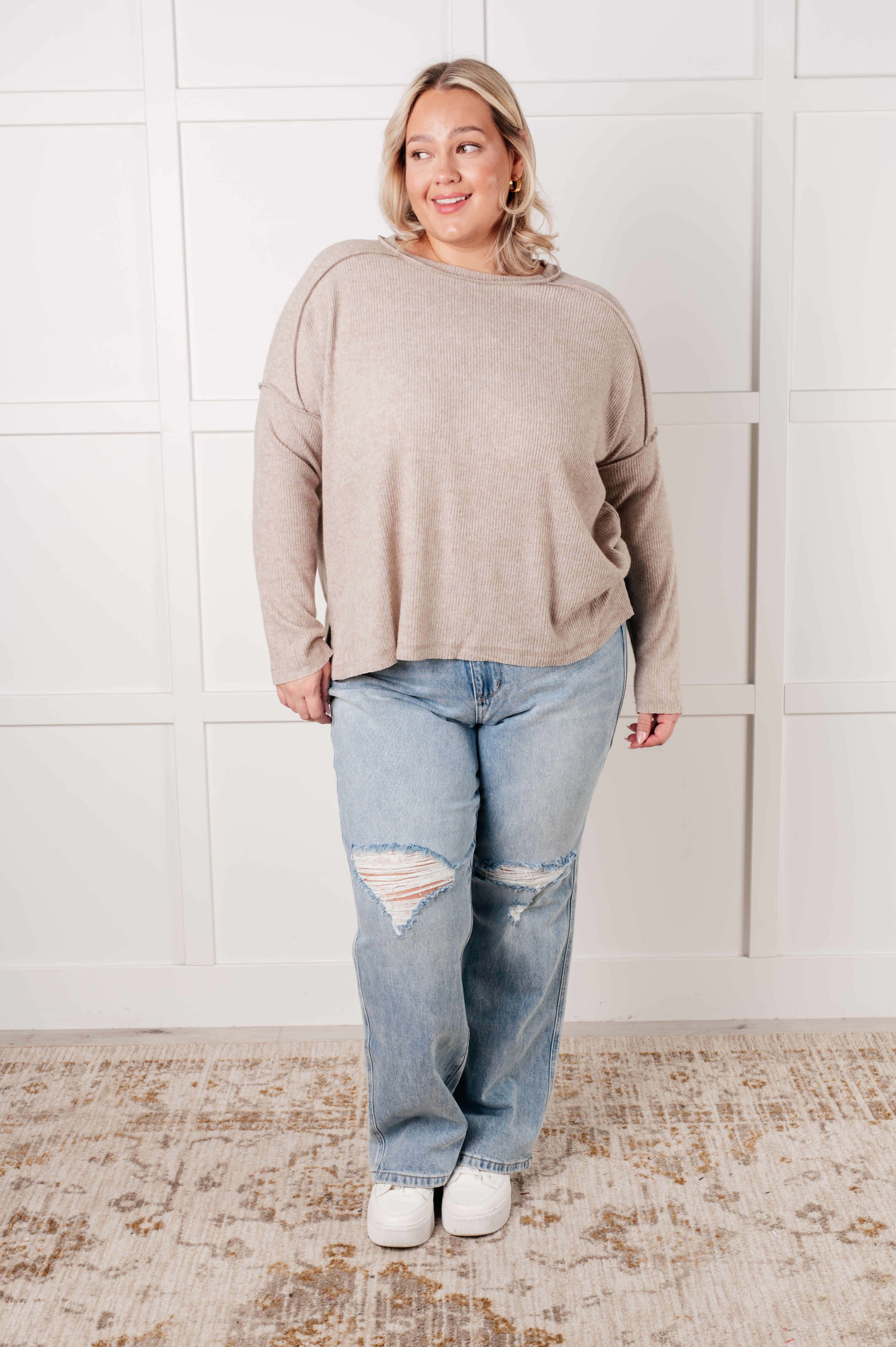 Plus-size woman wearing relaxed heather mocha ribbed sweater and distressed light blue jeans standing on patterned rug
