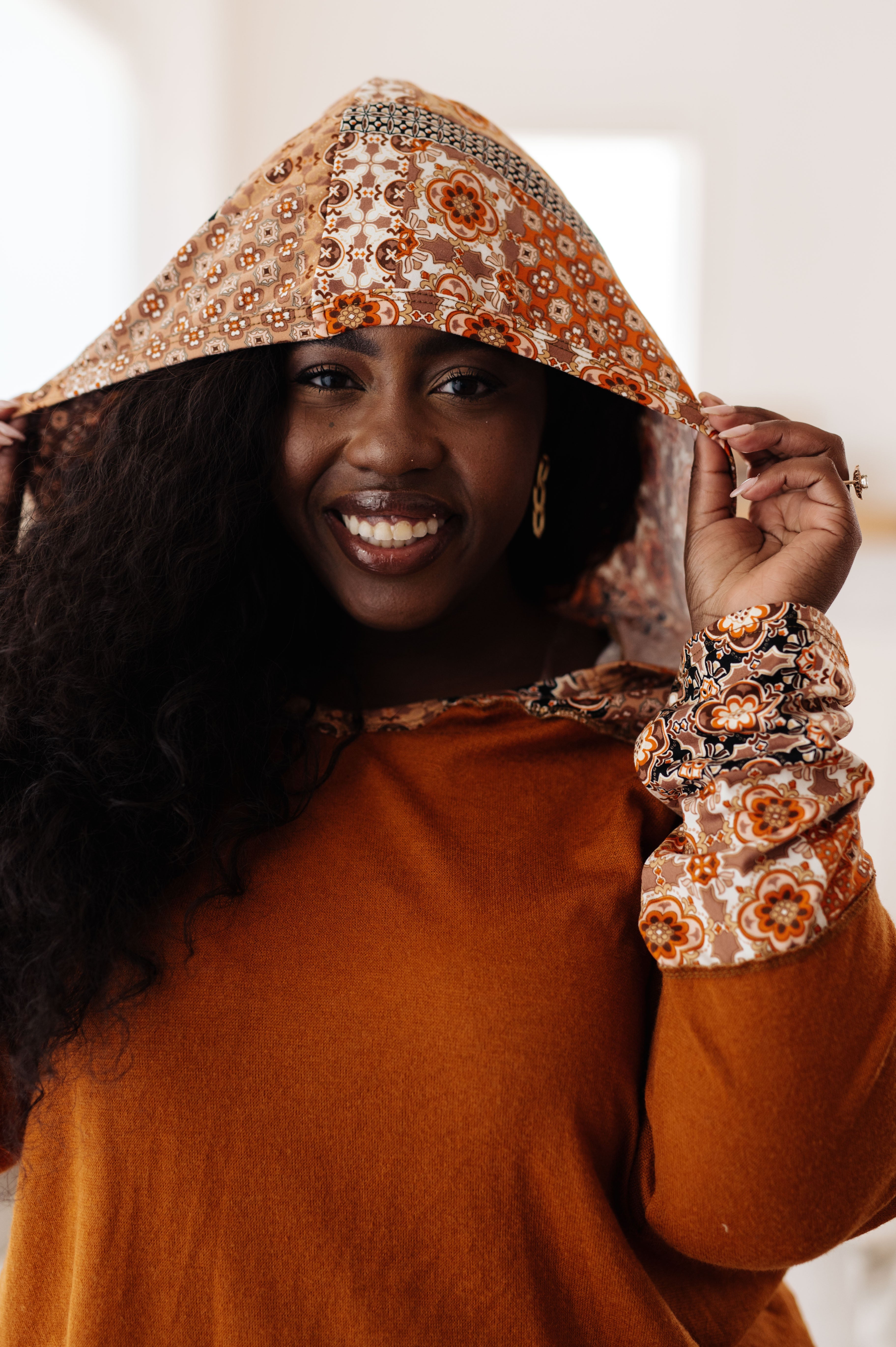 Smiling plus-size woman wearing rust-colored hoodie with mixed floral print hood and sleeves in warm indoor setting