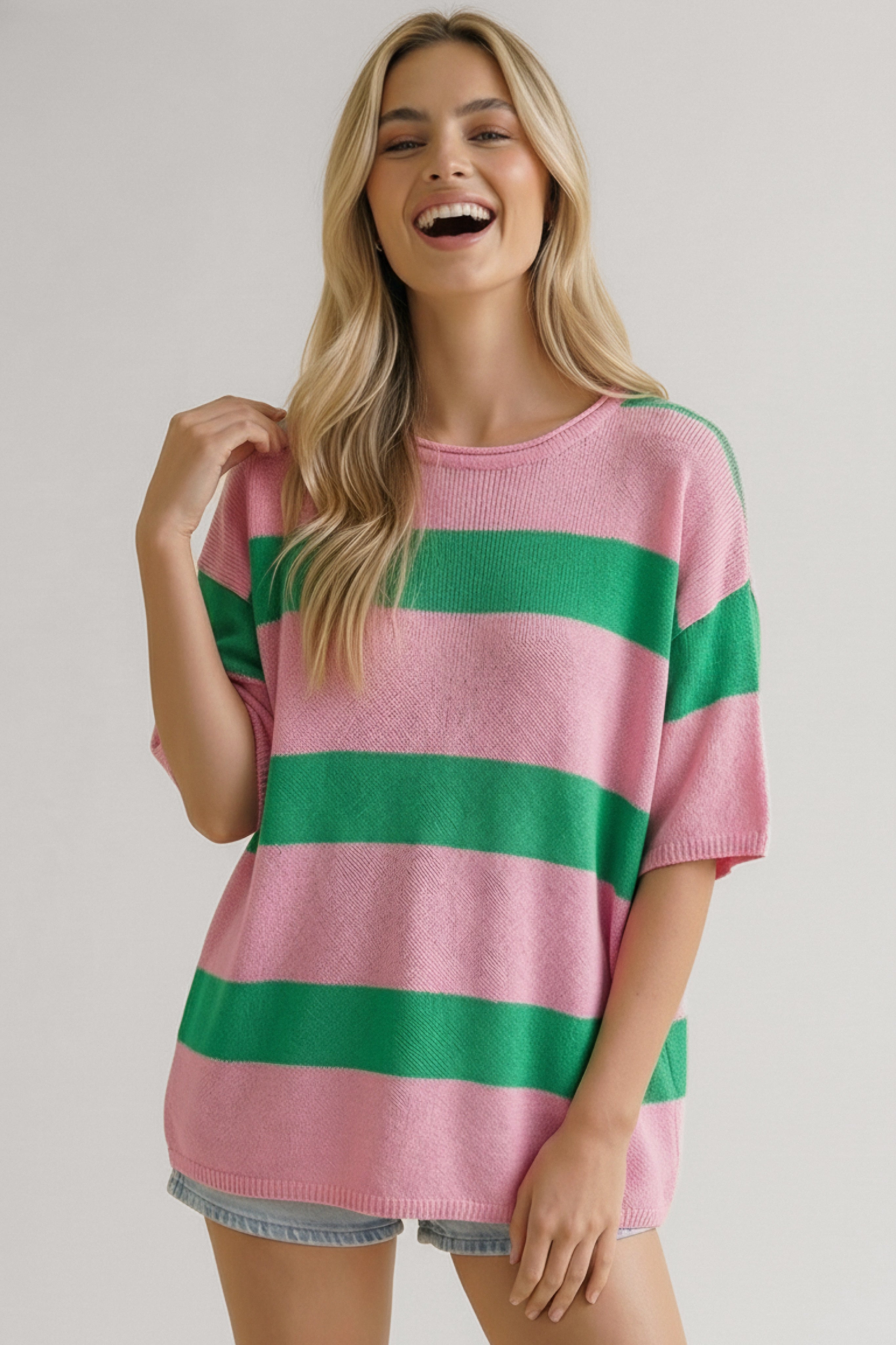 Smiling woman wearing a loose pink and green horizontally striped knit top with short sleeves and light denim shorts