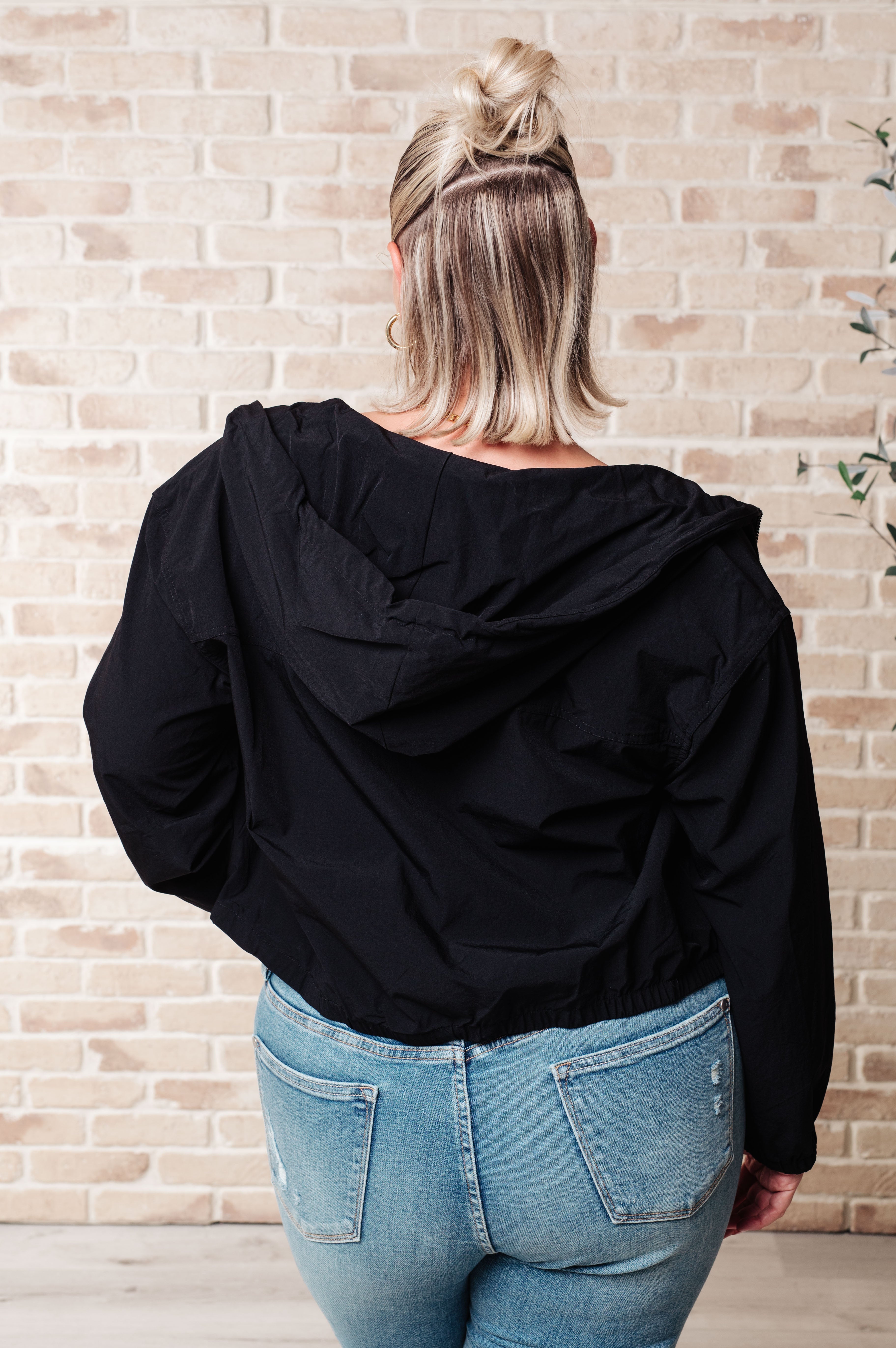Woman shown from behind wearing black zip-up hoodie with hood down paired with light blue distressed jeans indoors