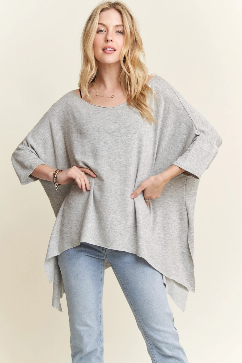 Woman wearing loose grey raw edge hem flowy top with three-quarter sleeves paired with light wash jeans