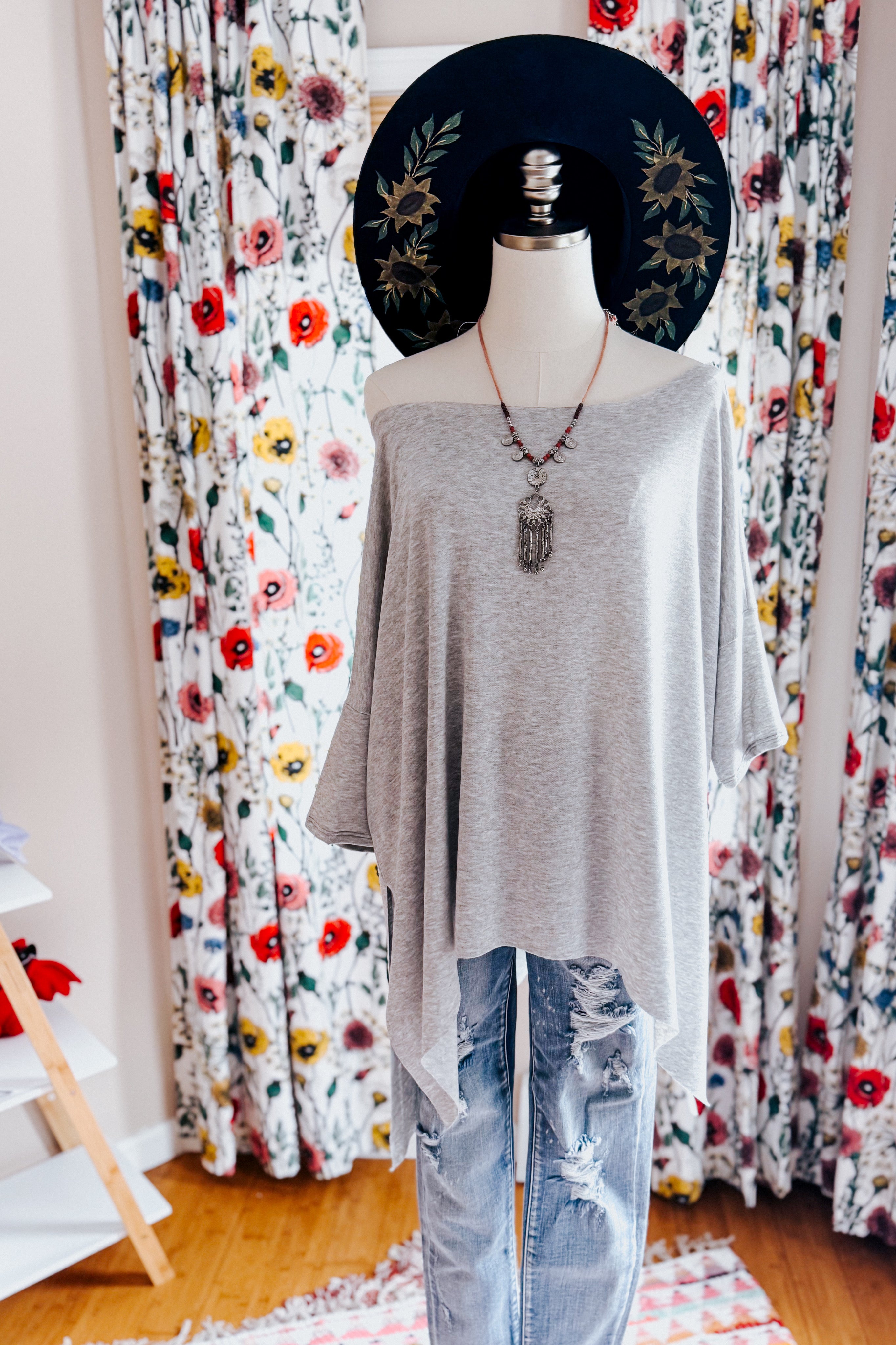 Mannequin dressed in a grey flowy top with raw edge hem paired with ripped light-wash denim jeans indoors