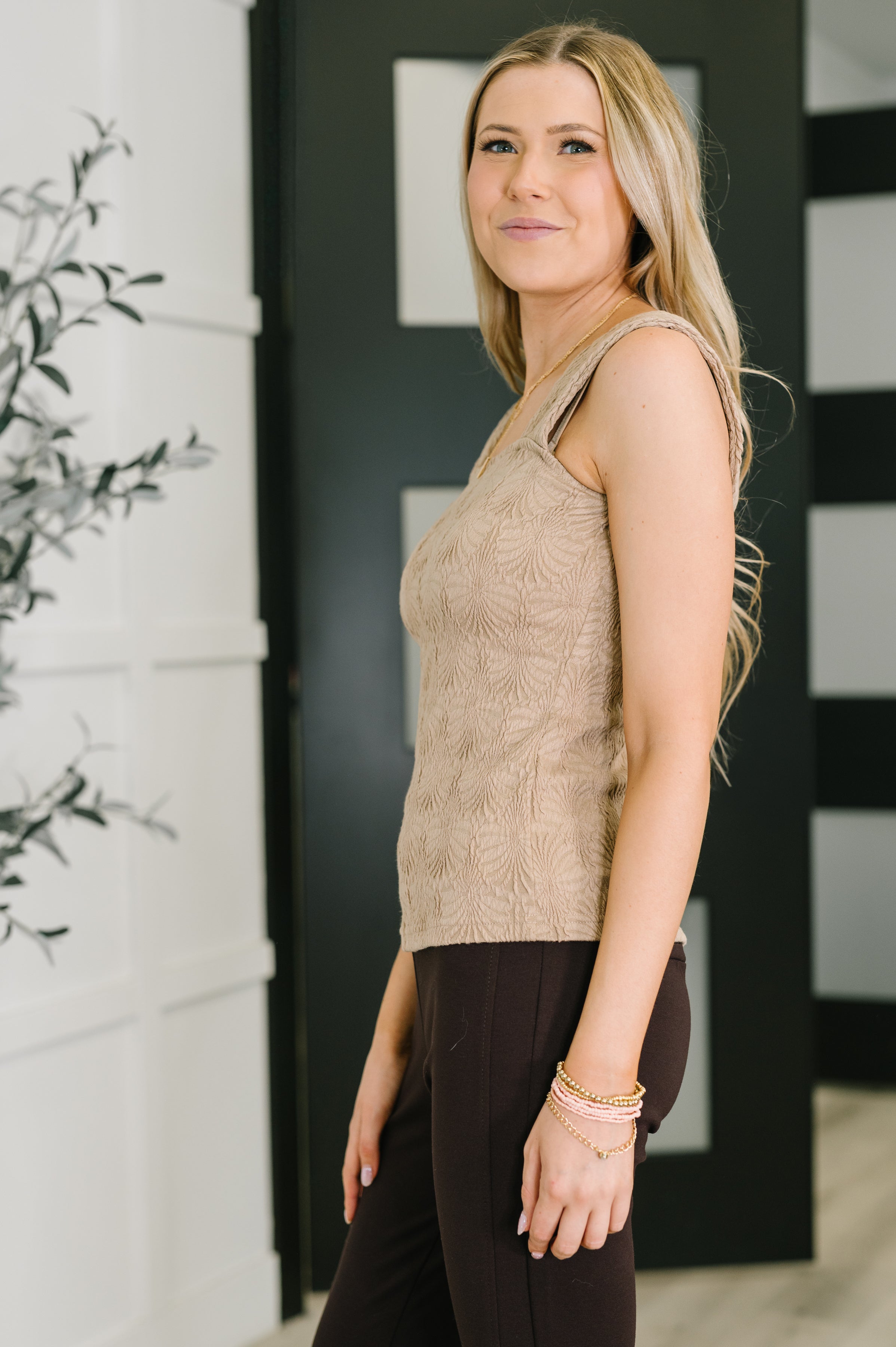 Woman wearing beige floral textured tank top paired with black pants and gold bracelets indoors