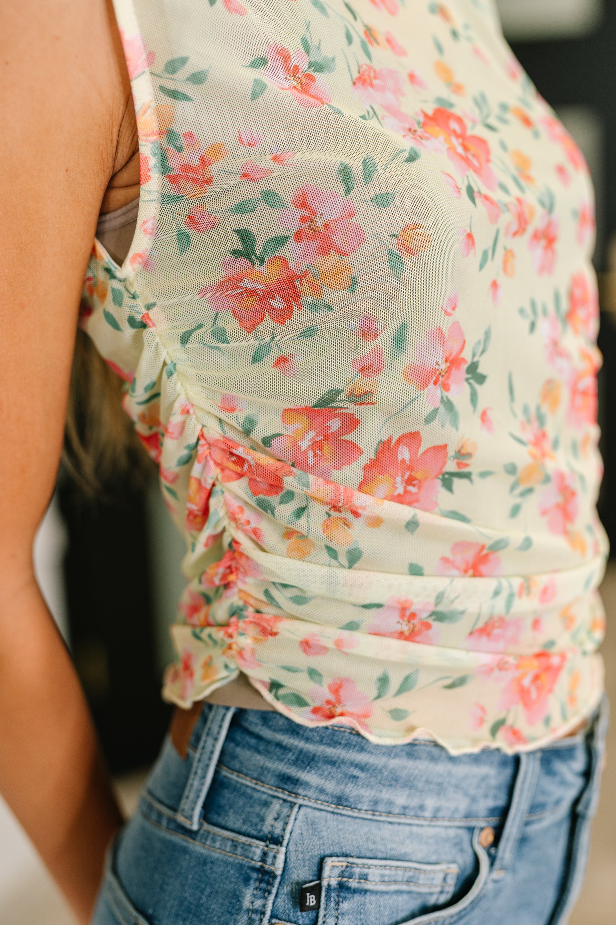 Close-up of sheer floral layering top in soft chartreuse with ruched side detail paired with light blue denim jeans