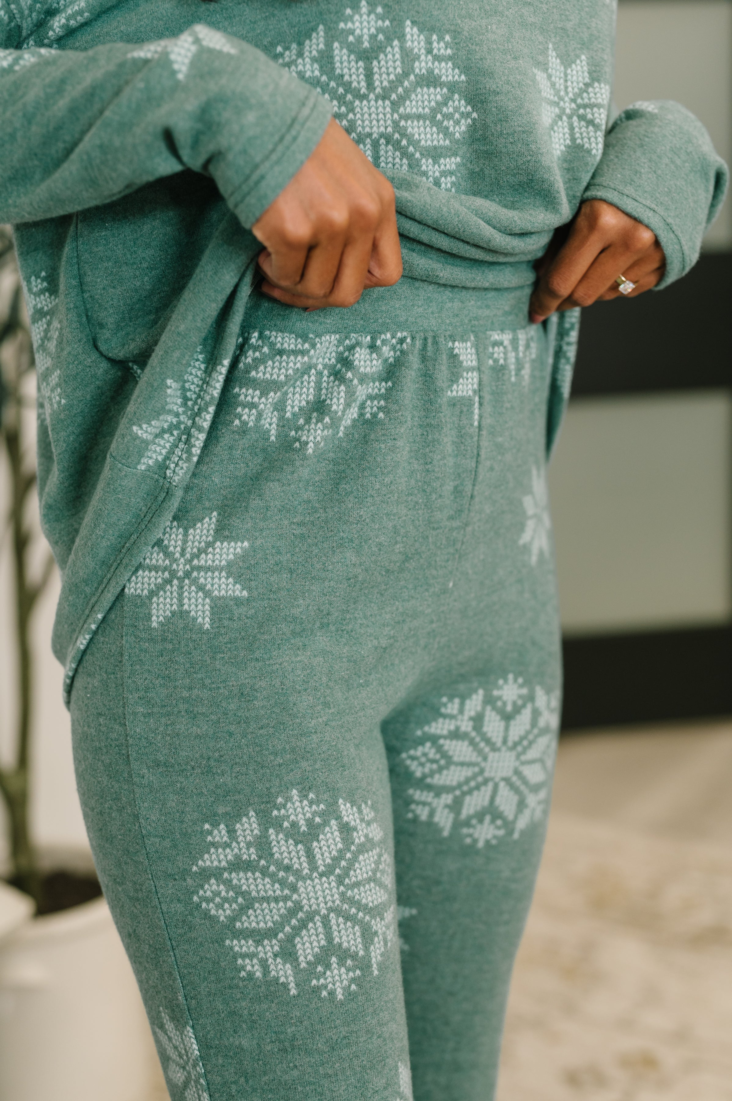 Close-up of person adjusting green knit pajama pants with white snowflake pattern indoors