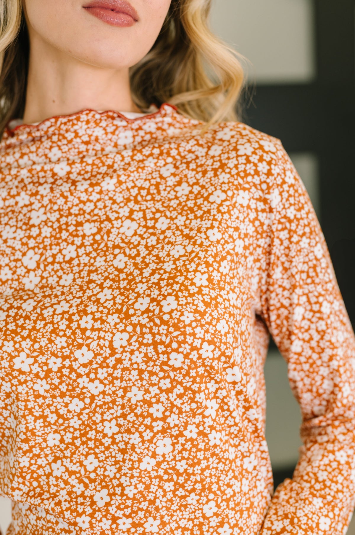 Close view of a woman wearing an orange floral long sleeve top with a softly ruffled neckline and fitted silhouette