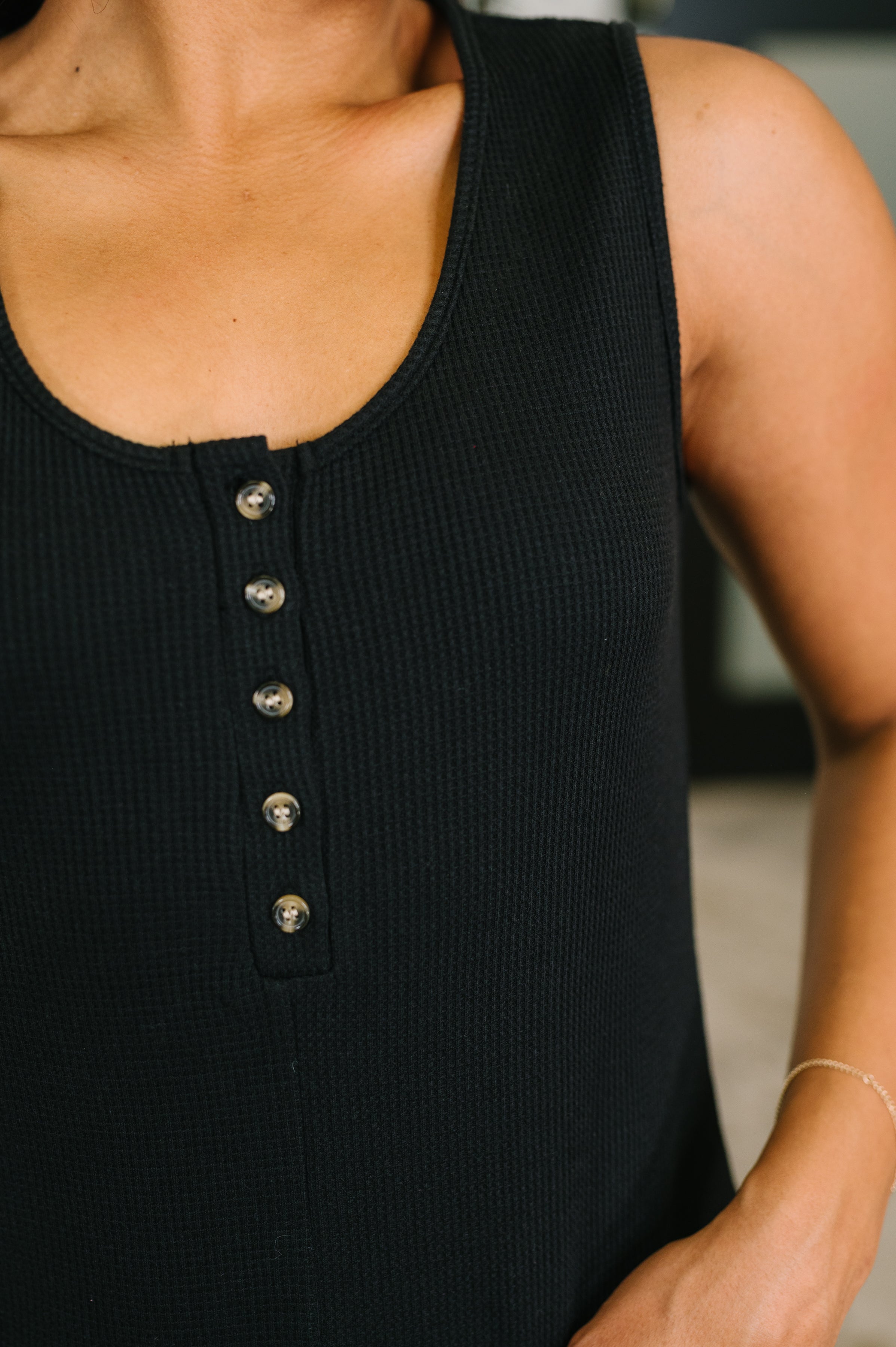 Close-up of black textured sleeveless Henley romper with small buttons and scooped neckline on model