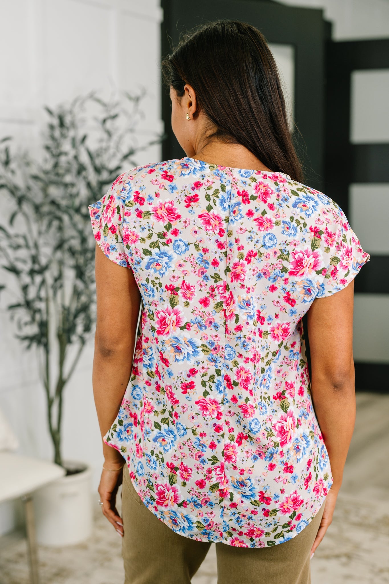 Back view of woman wearing pink floral print blouse with blue and red flowers in casual indoor setting
