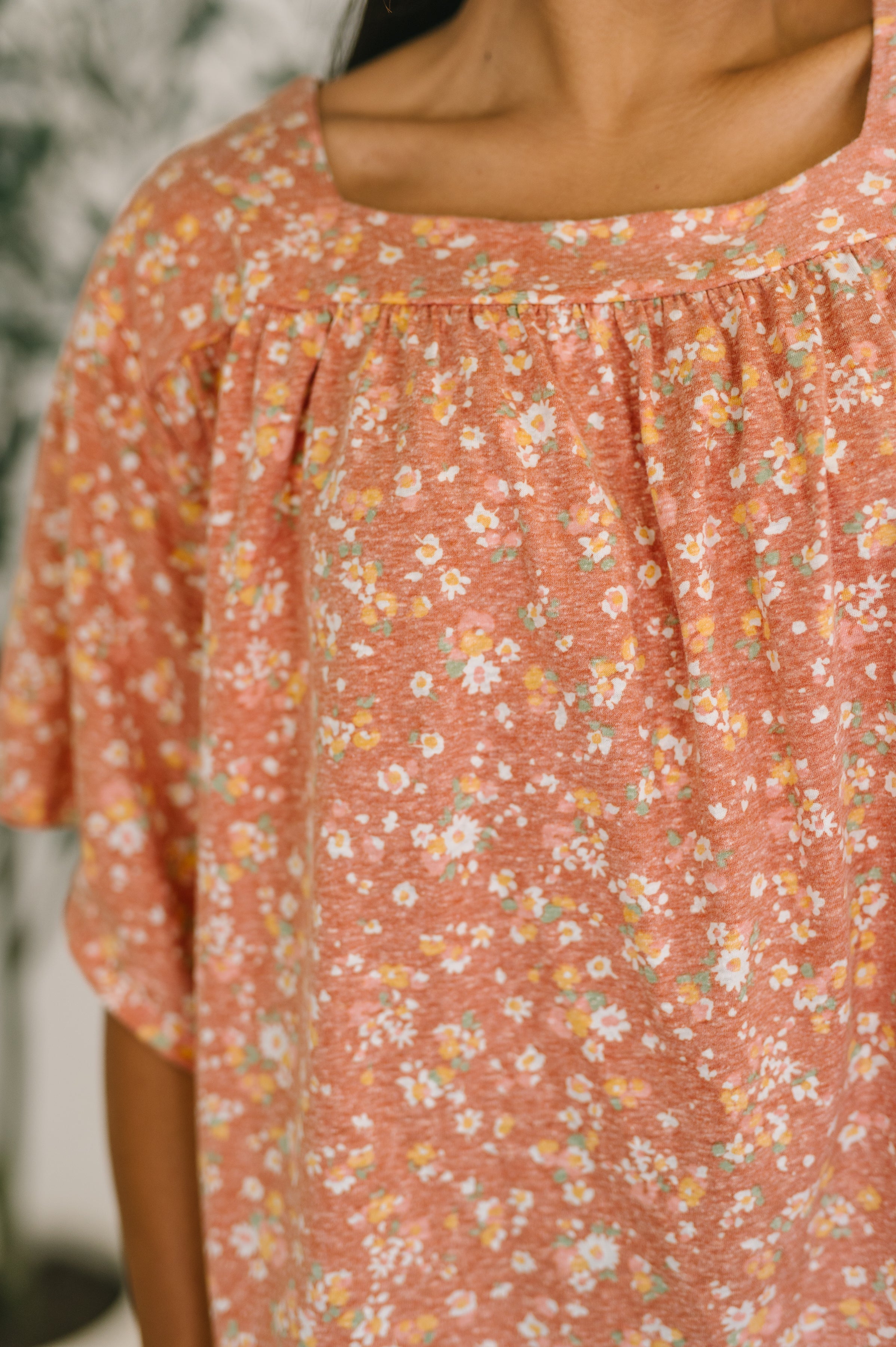 Close-up of a pink floral top with small white and yellow flowers and a square neckline on a woman