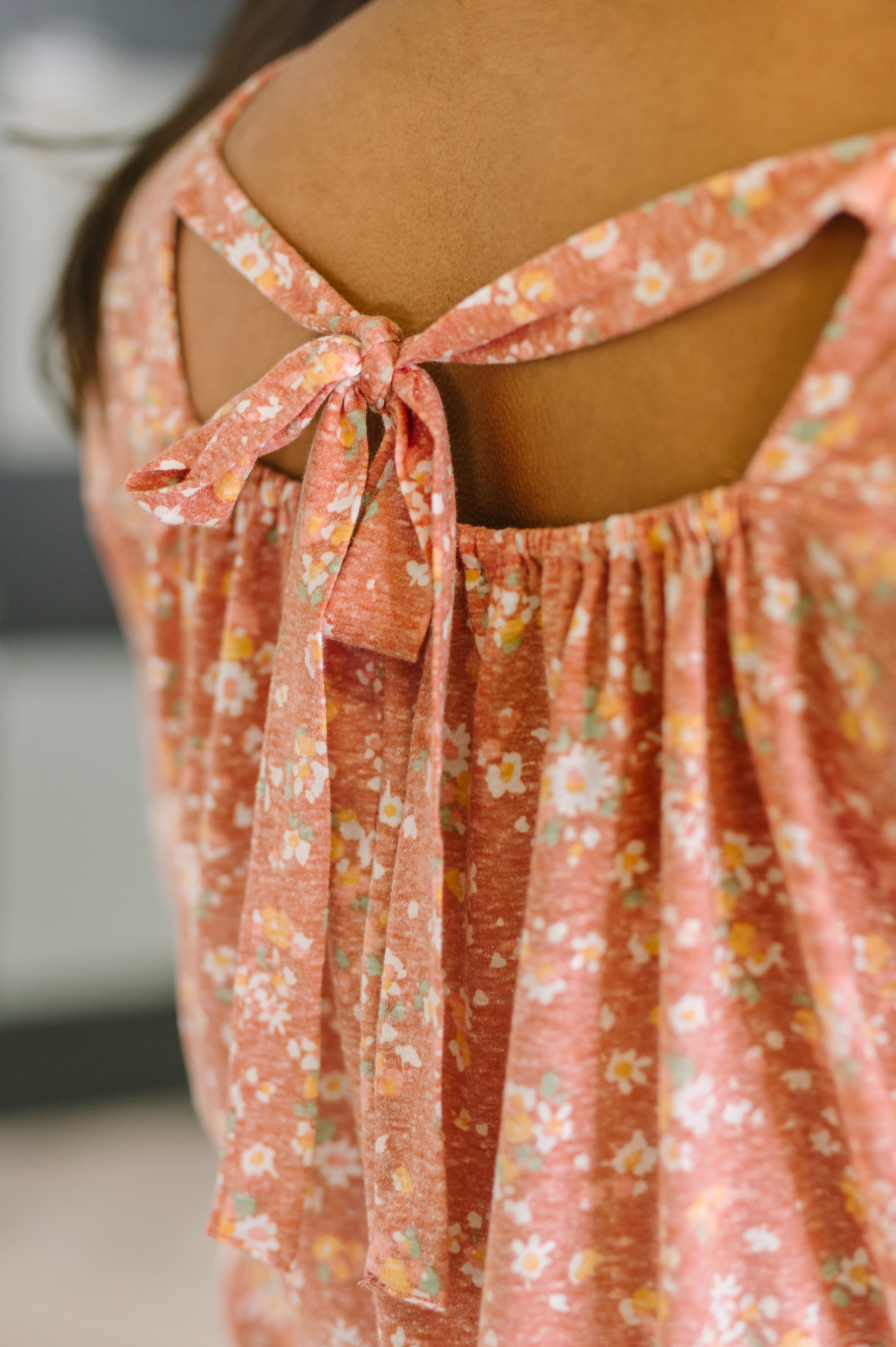 Close-up of a back detail on a pink fabric with white and yellow floral pattern tied into a bow on brown skin