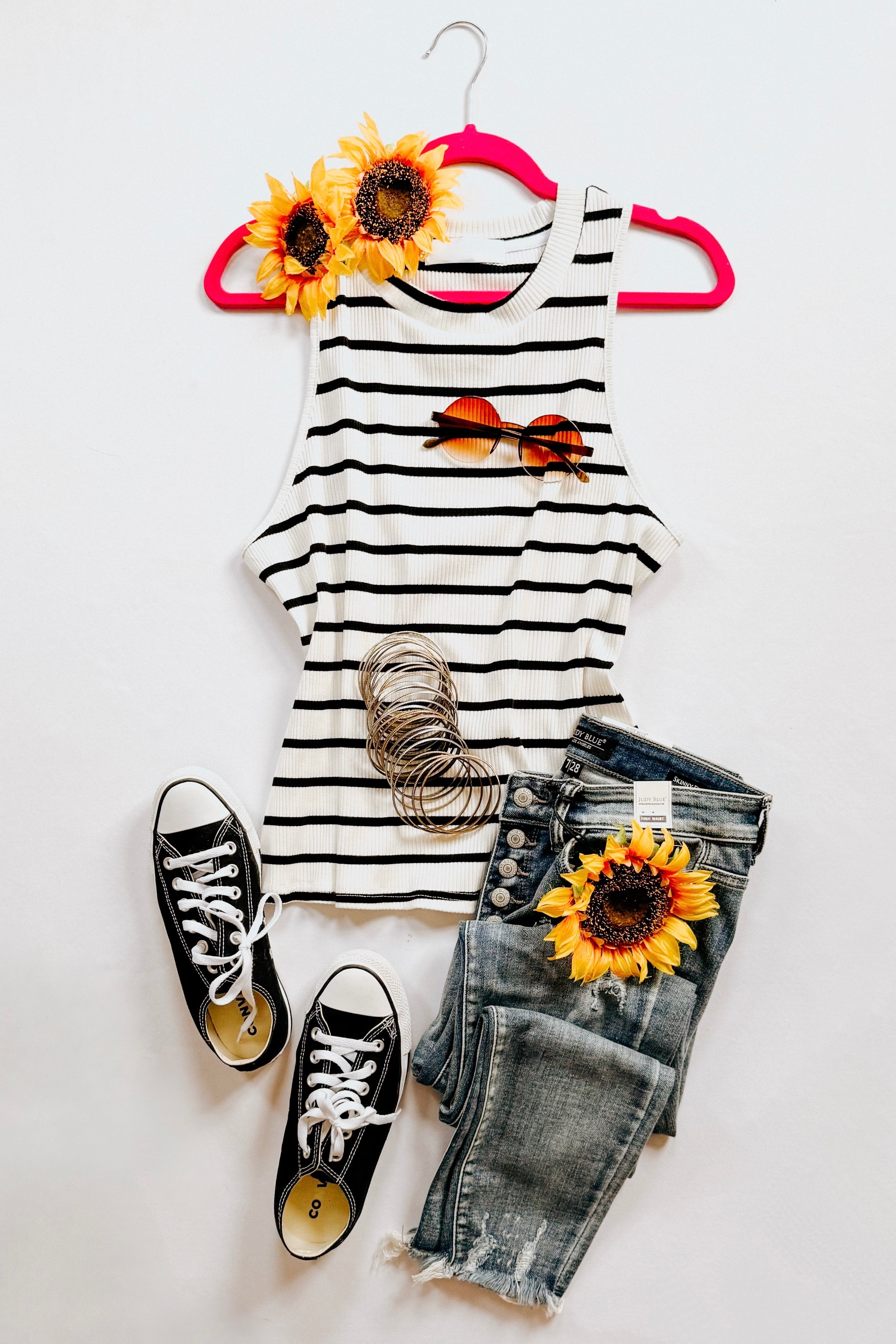Ivory ribbed halter tank with black stripes styled with distressed jeans, black sneakers, sunglasses, and sunflower accents on white background