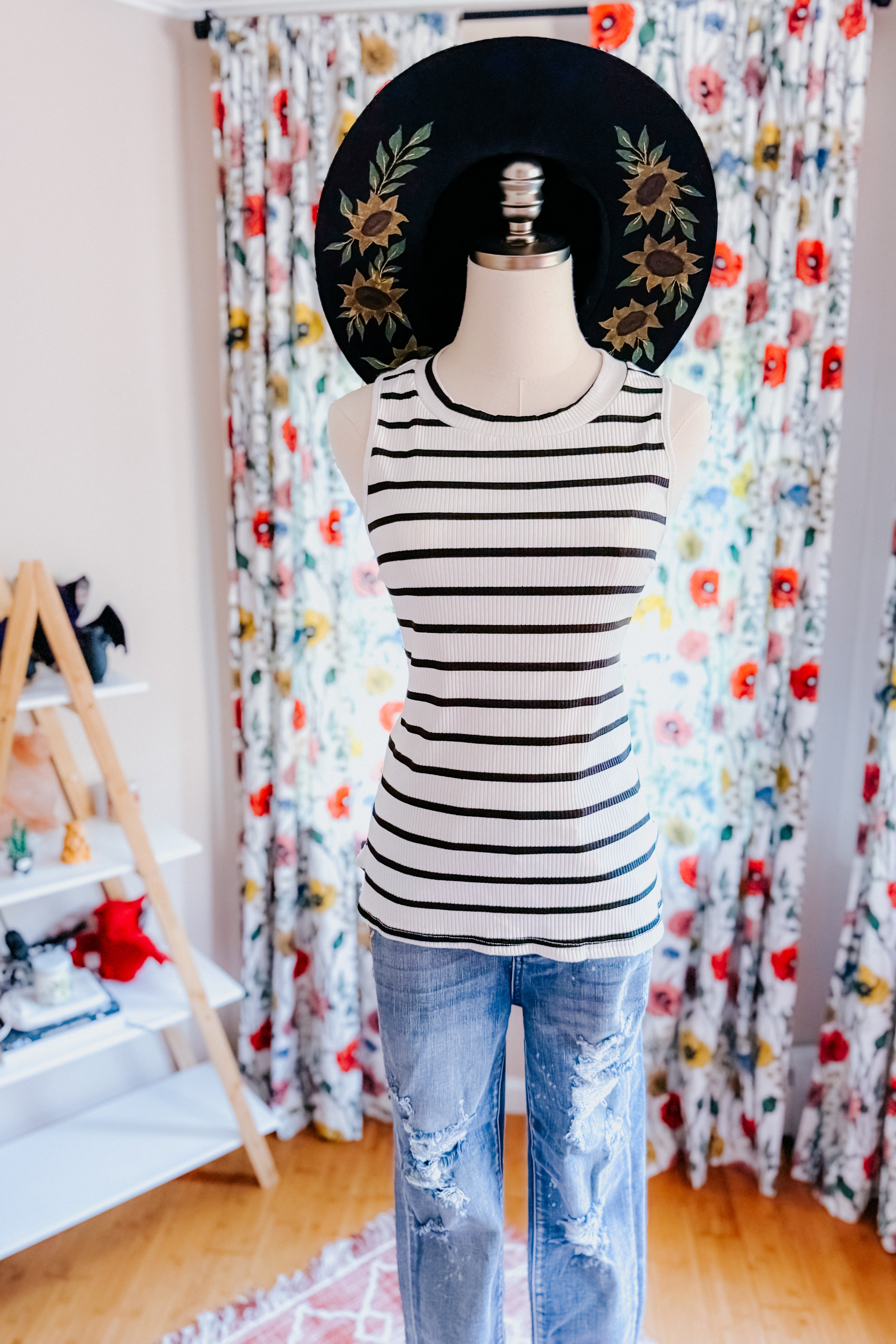 Striped ribbed sleeveless top paired with distressed blue jeans and a black wide-brimmed hat with sunflower embroidery indoors