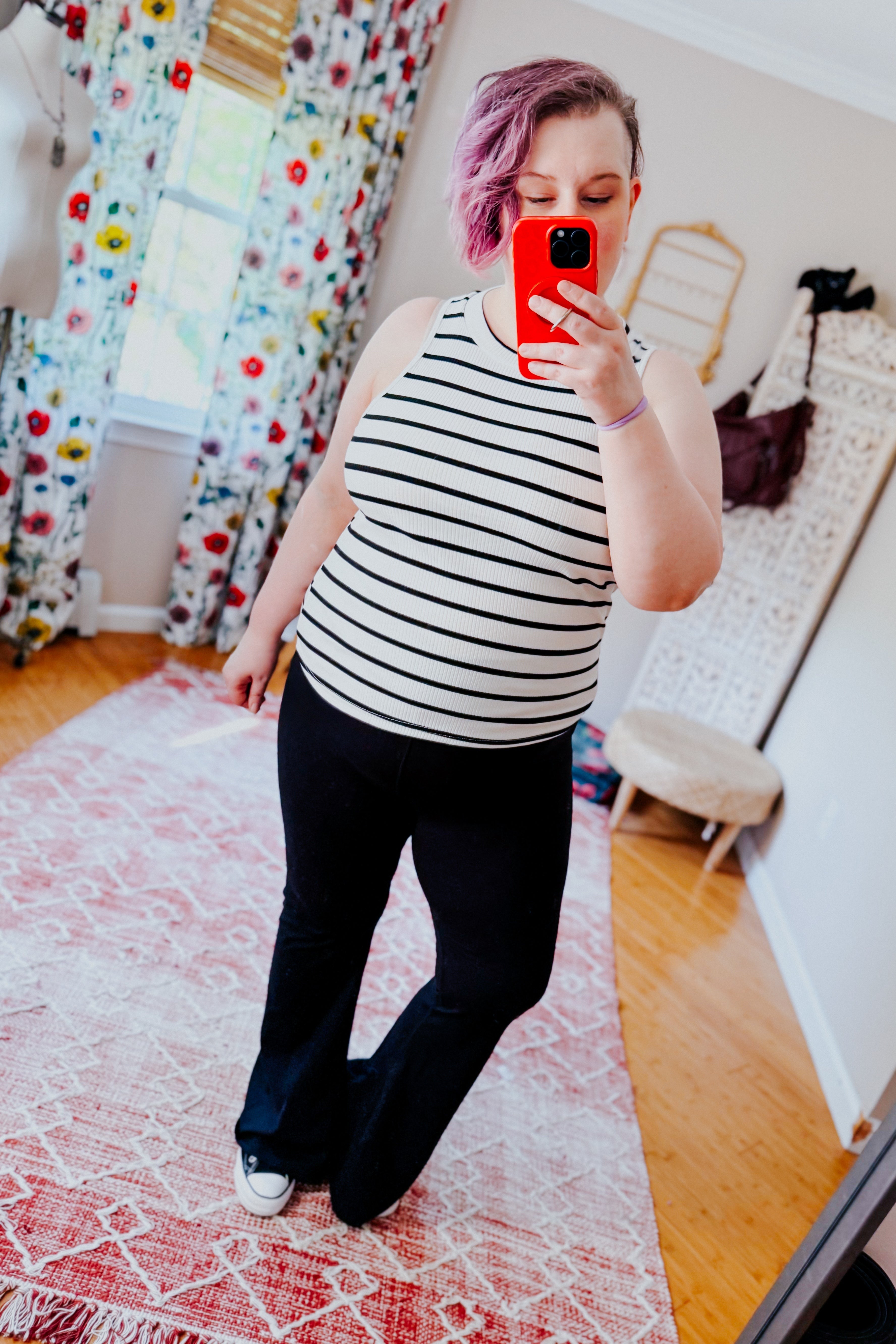 Woman with short purple hair wearing a striped fitted halter top and black pants taking a selfie indoors