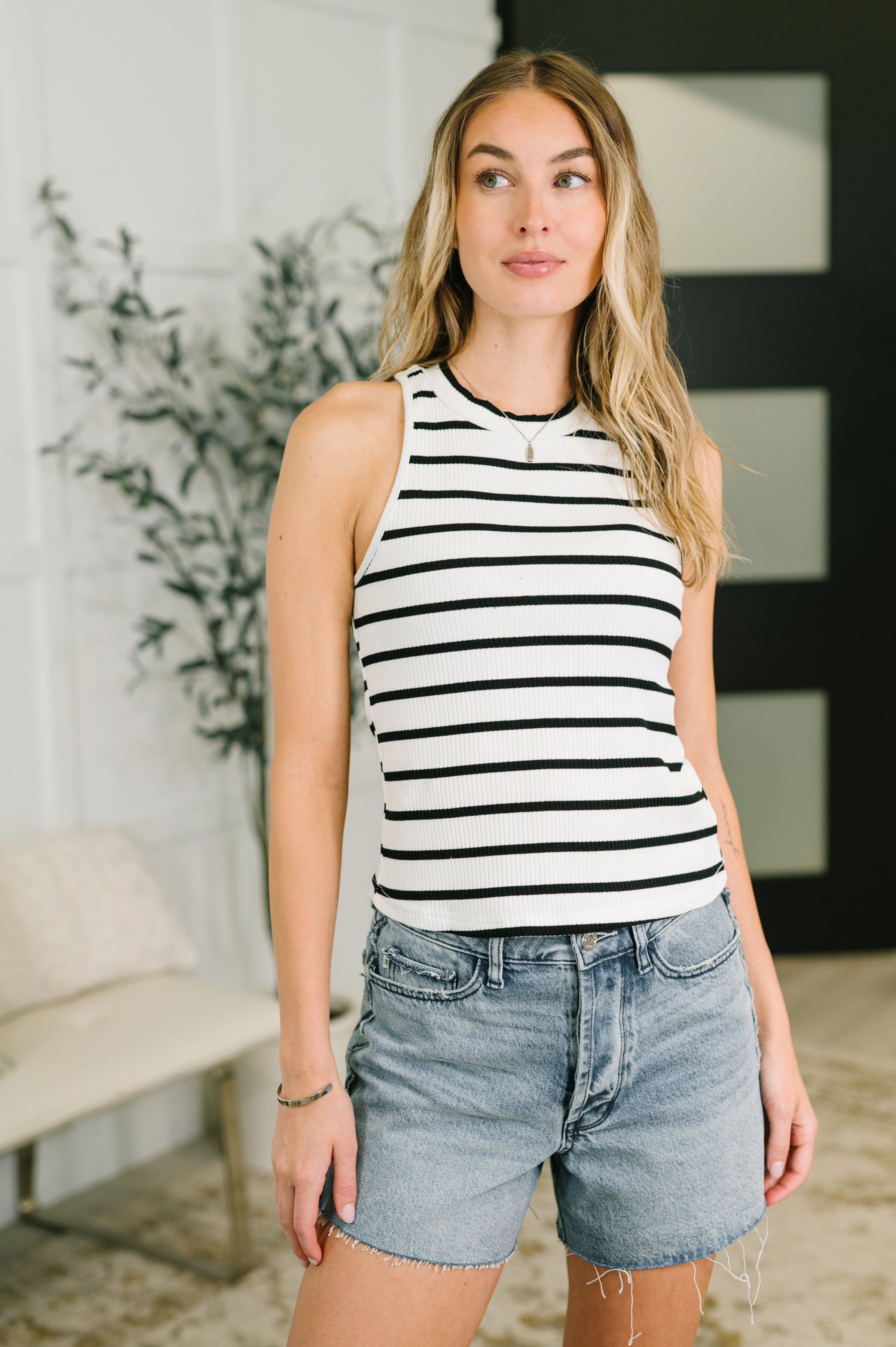 Woman wearing ribbed black and white striped halter tank paired with light wash denim shorts indoors