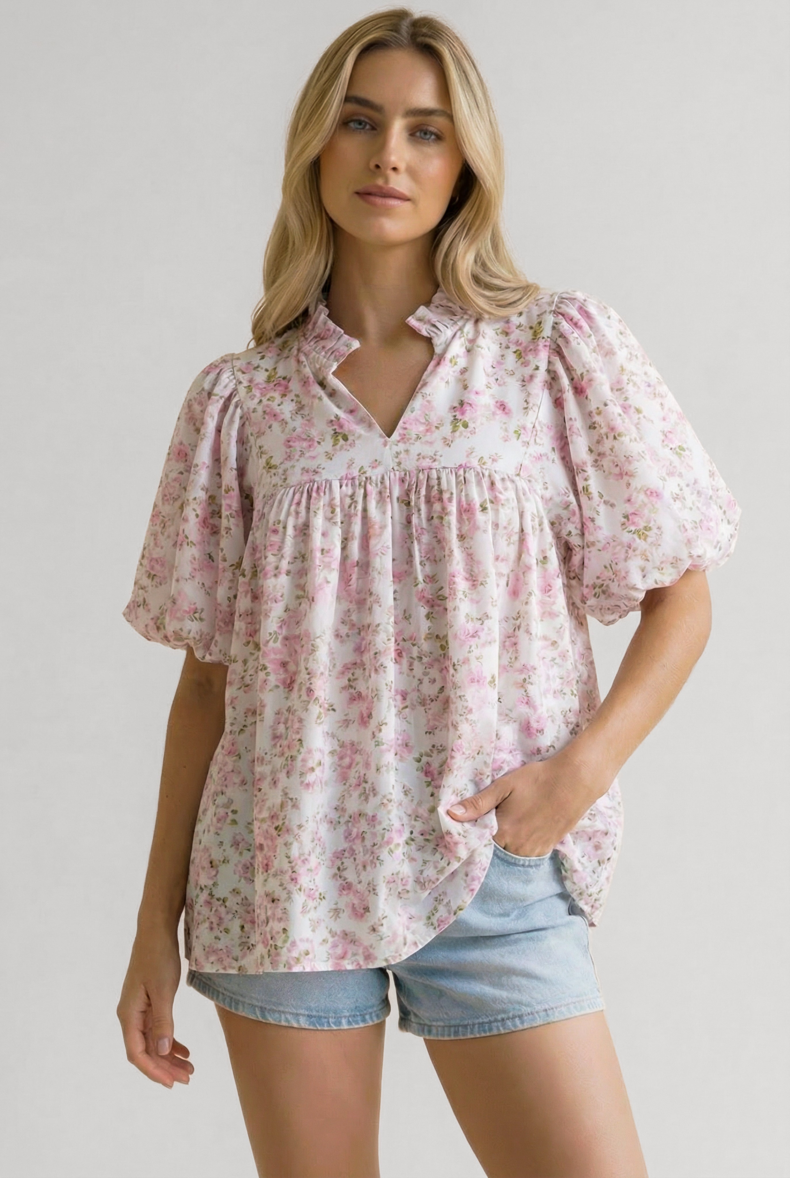 Woman wearing a relaxed pink floral blouse with puffed sleeves and a ruffled collar paired with light denim shorts