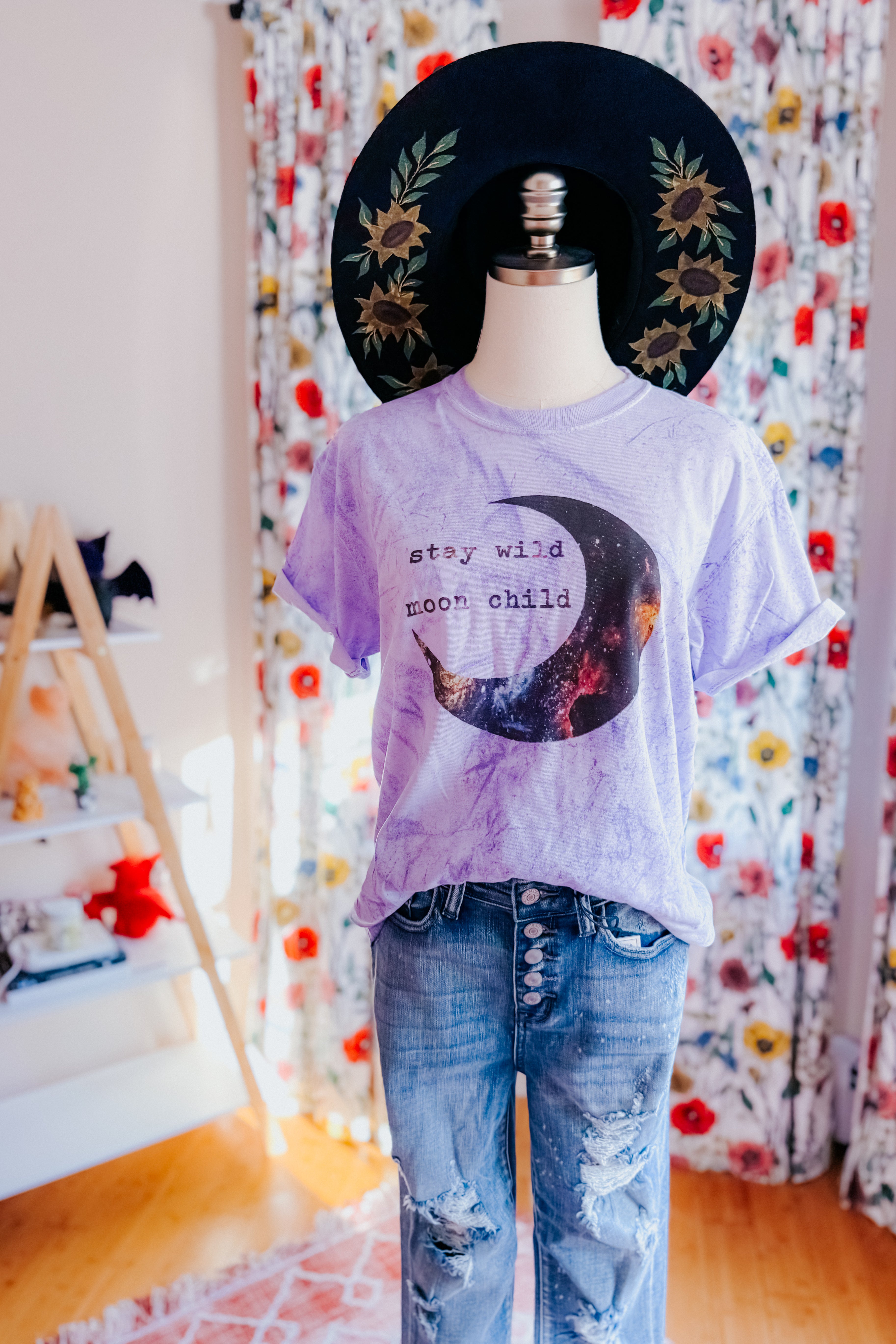 Mannequin wearing a purple tie-dye tee with moon graphic and text paired with distressed button-fly jeans and black wide-brim hat