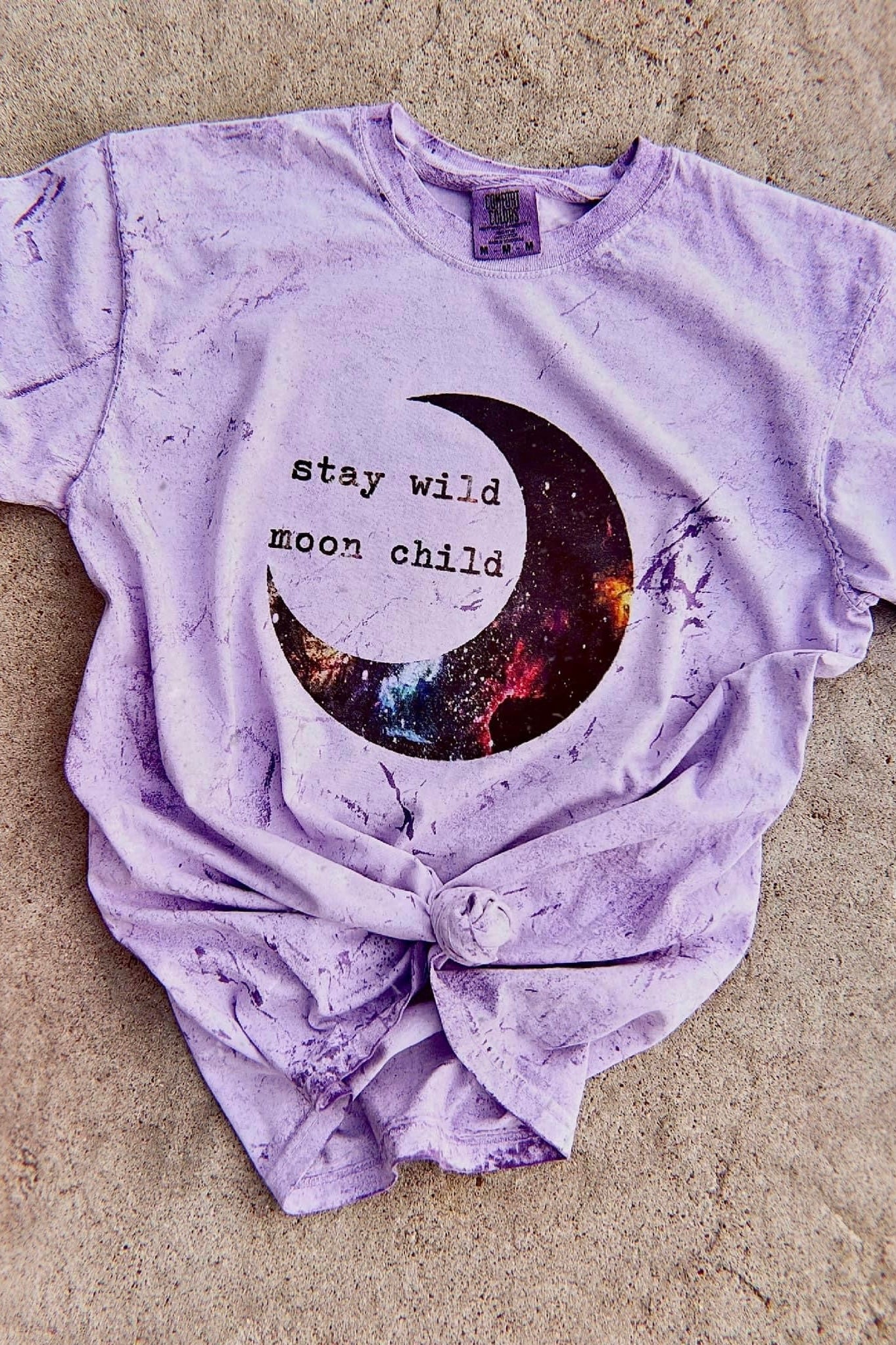 Purple tie-dye tee with celestial crescent moon graphic and "stay wild moon child" text, knotted at hem