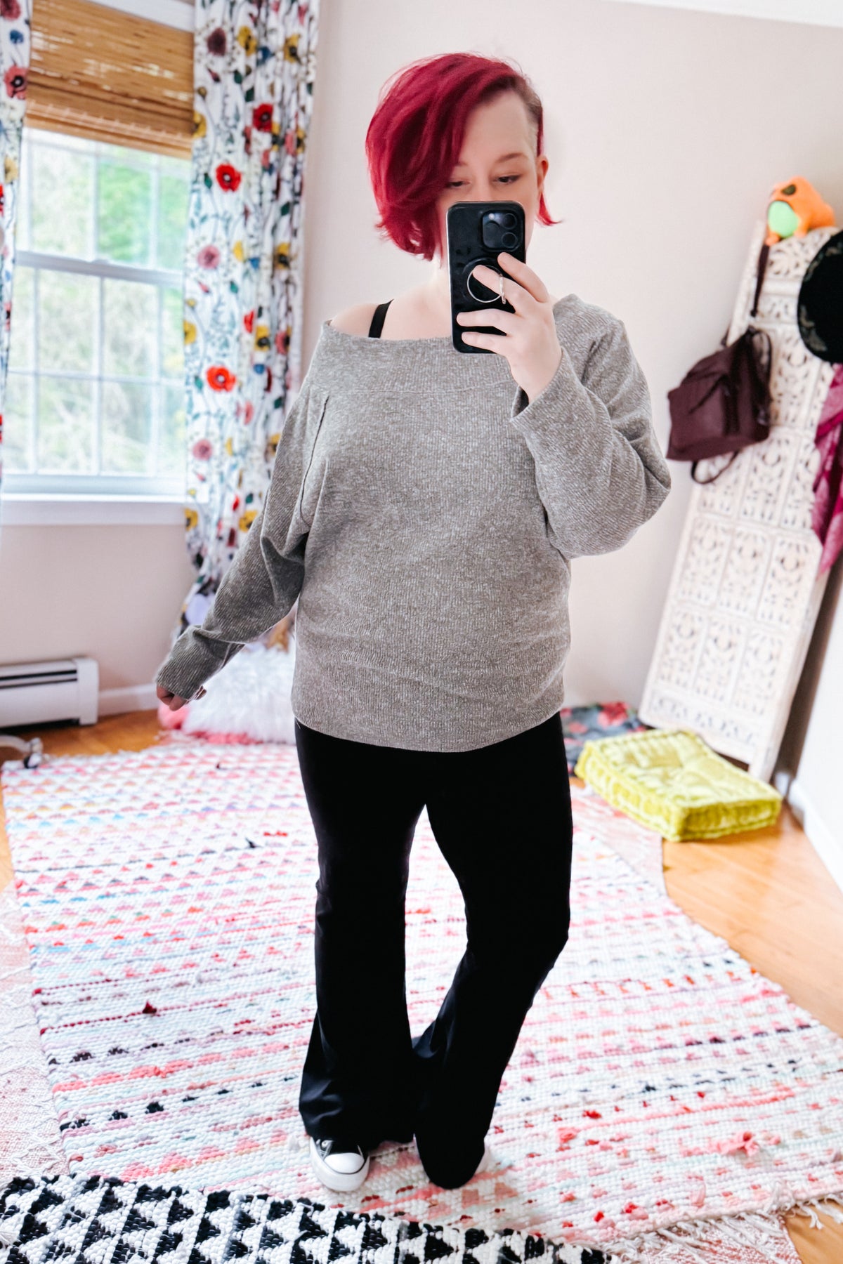 Woman taking a mirror selfie in a grey textured knit boat neck top with dolman sleeves and an off shoulder neckline with black pants