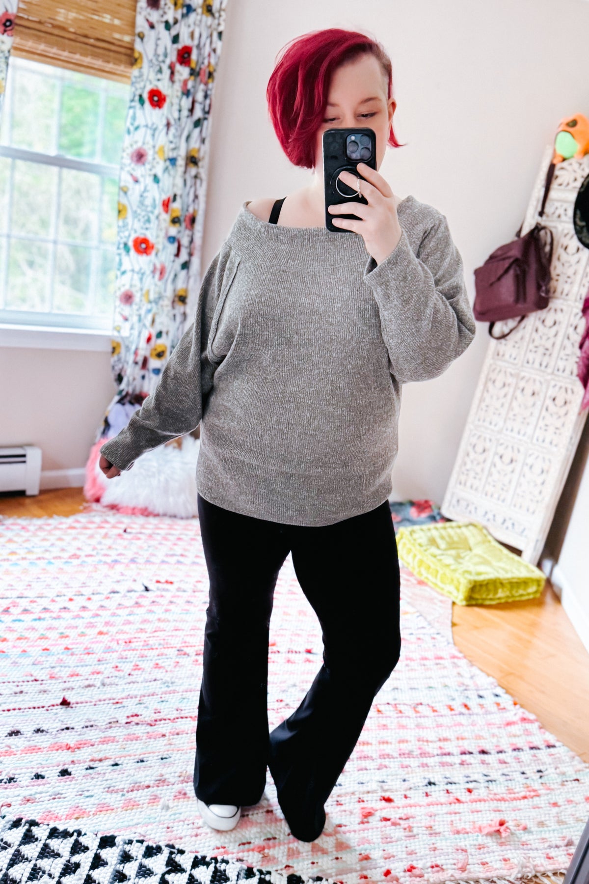 Woman taking a mirror selfie in a grey textured knit boat neck top with dolman sleeves, paired with black pants indoors