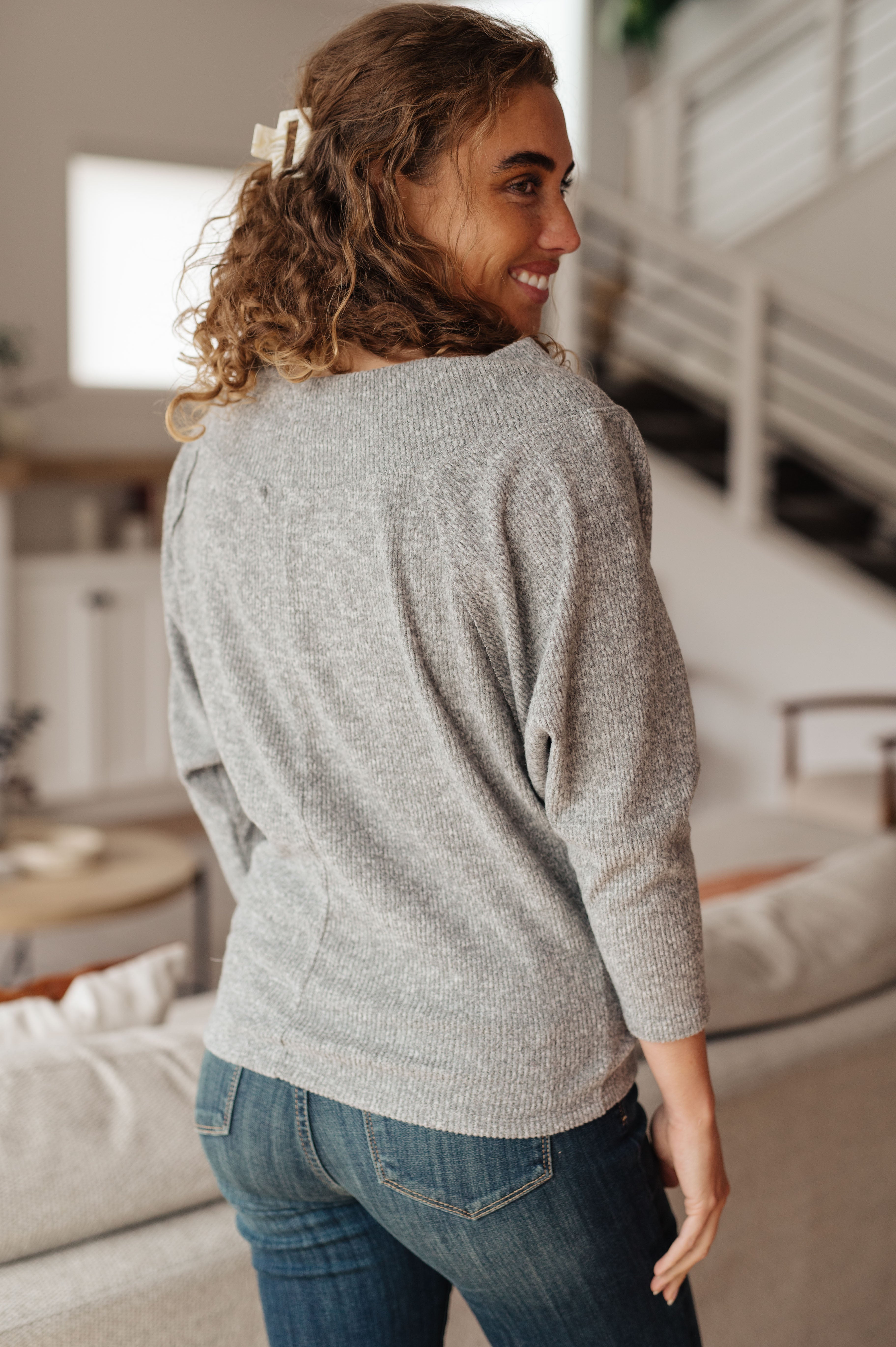 Woman wearing a grey textured long sleeve top with relaxed fit and cropped sleeves, standing indoors with casual smile