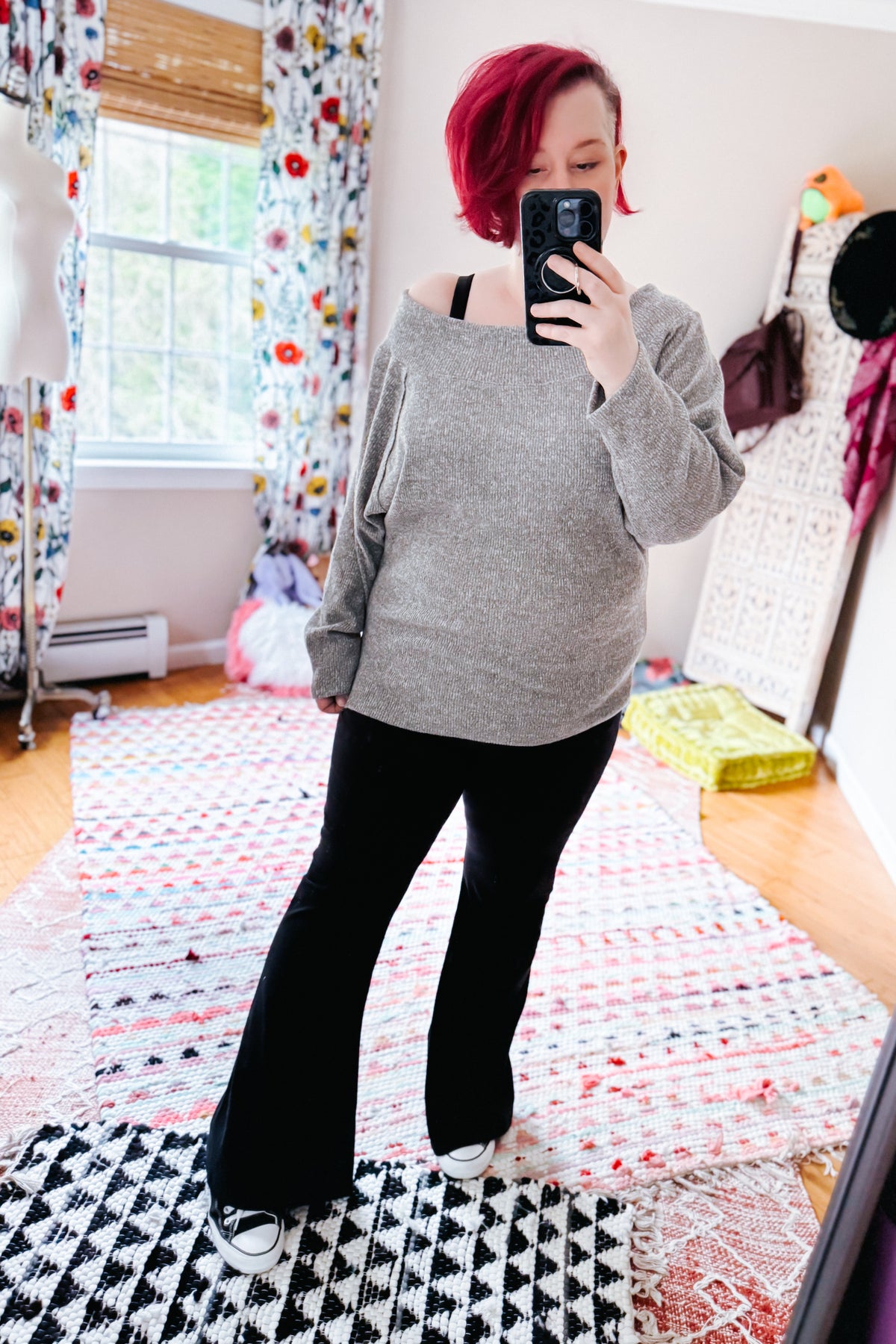 Woman taking a mirror selfie in a grey textured knit boat neck top with dolman sleeves and black pants indoors