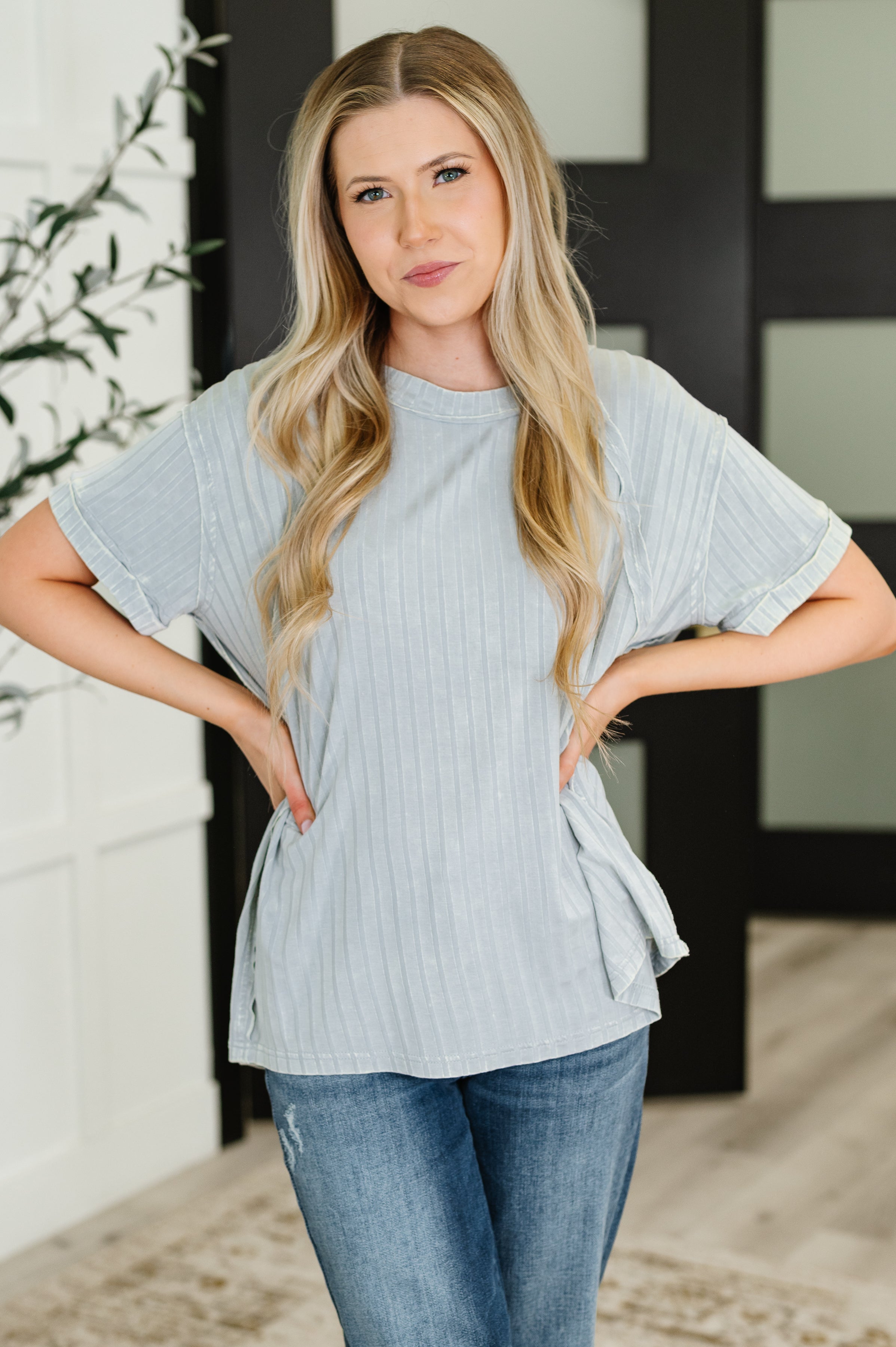 Woman wearing light grey mineral wash top with short sleeves paired with medium wash jeans indoors