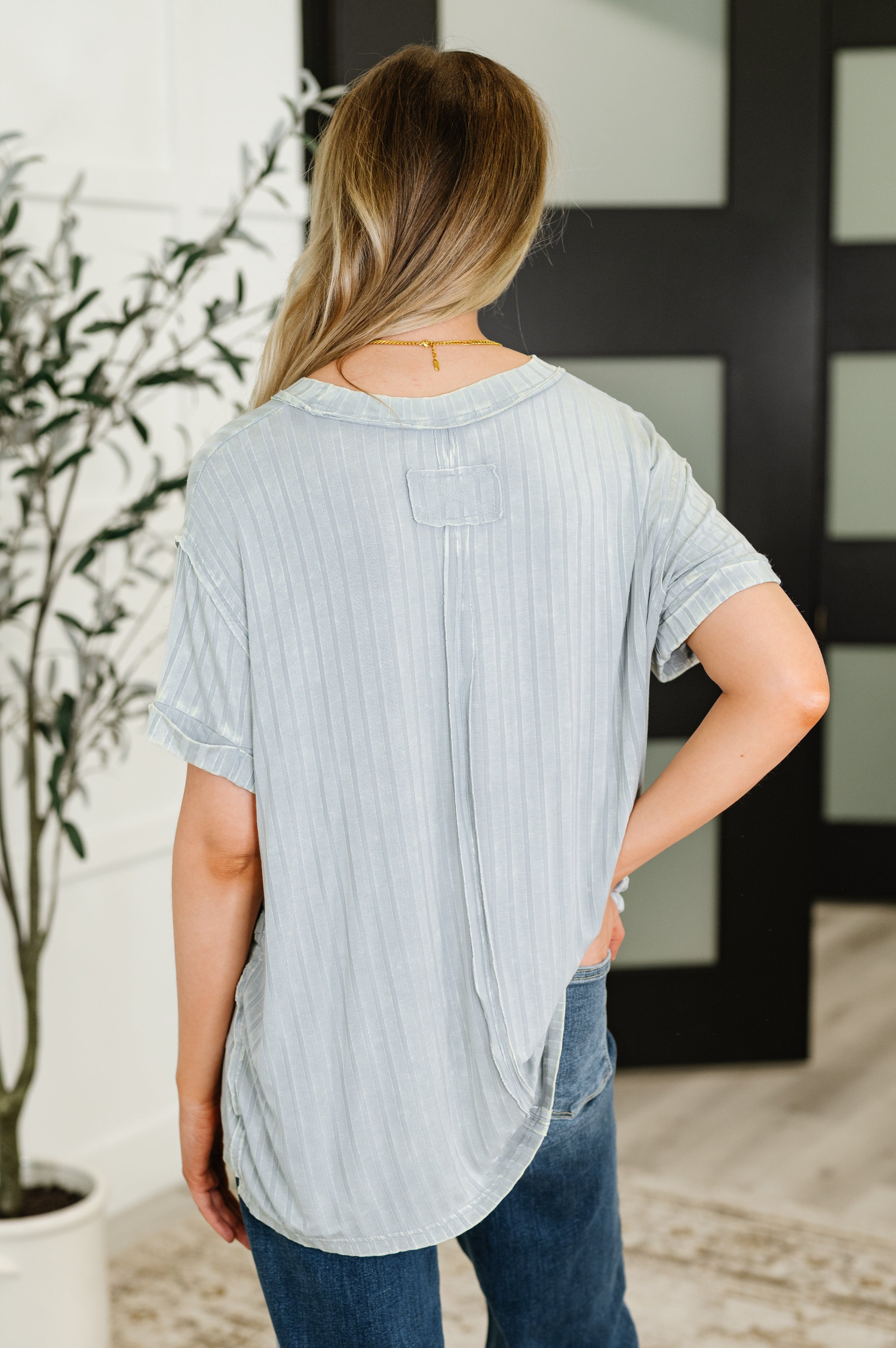 Woman wearing light grey mineral wash top with subtle vertical stripes paired with denim jeans viewed from behind