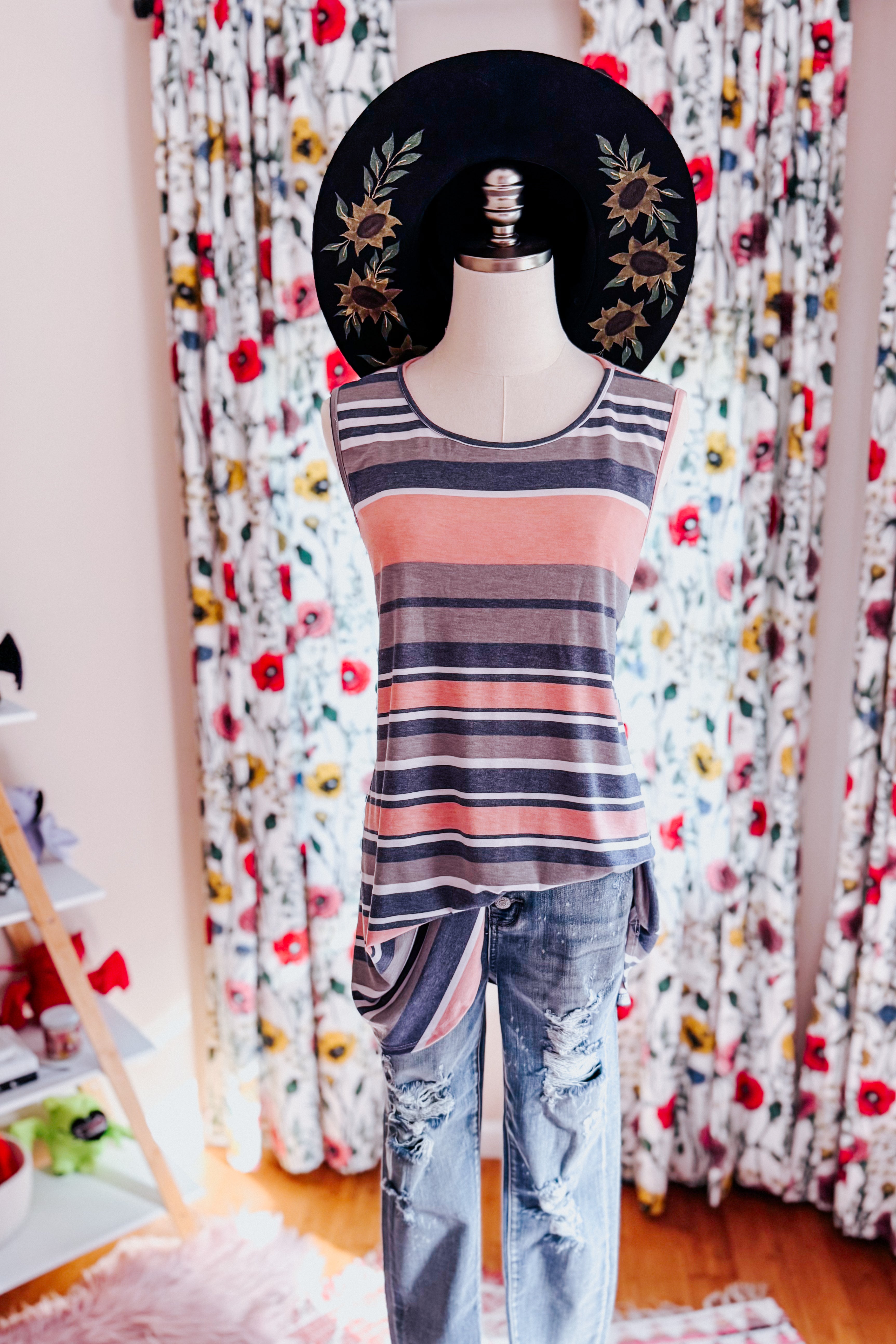 Striped pink and gray sleeveless top paired with distressed jeans and a black wide-brim hat with floral embroidery