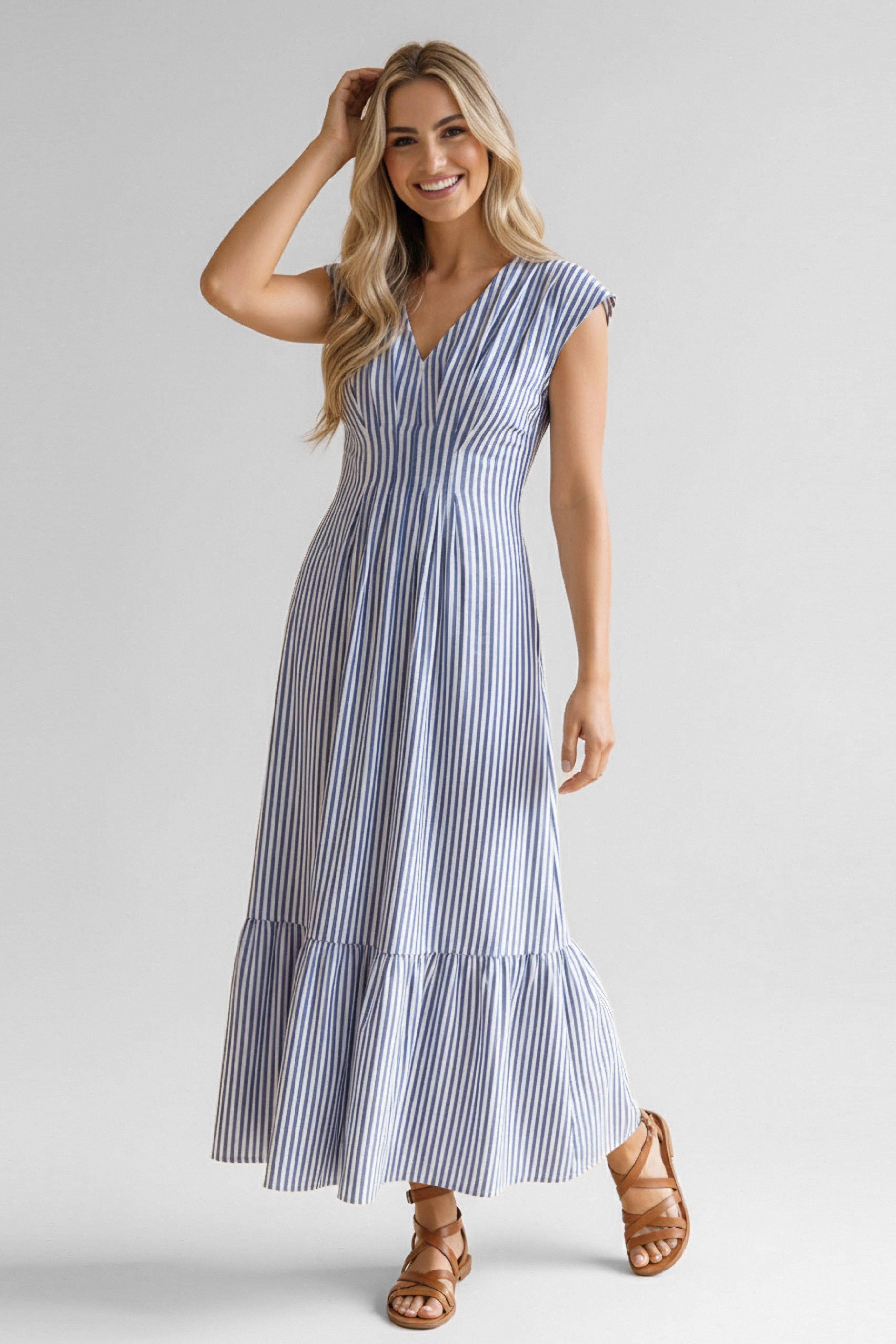 Smiling woman wearing blue striped midi dress with cap sleeves and ruffled hem paired with brown sandals