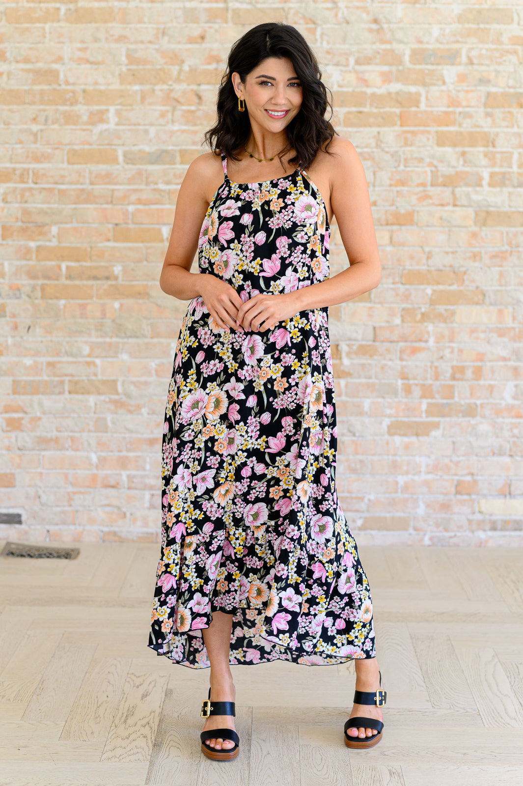 Woman wearing a black halter dress with pink and yellow floral print paired with black open-toe heels indoors