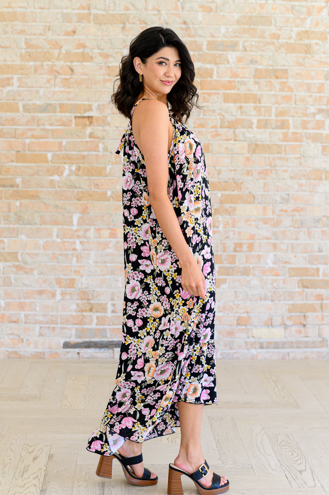 Woman wearing a black halter dress with pink and peach floral pattern paired with black heeled sandals indoors