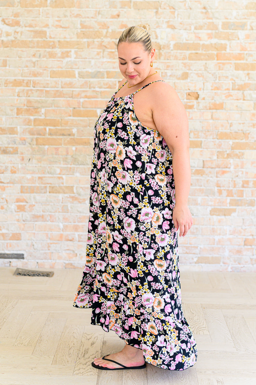 Side view of woman in a black halter dress featuring pink and peach floral patterns paired with black sandals indoors
